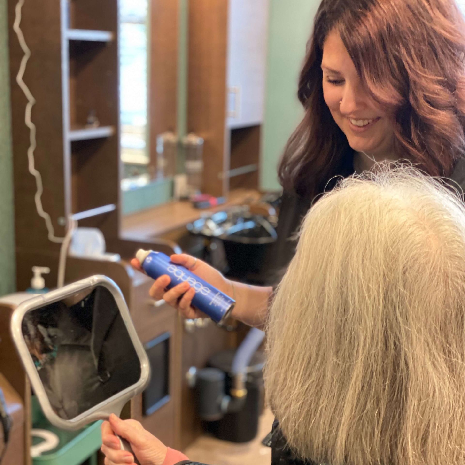 hairstylist applying hairspray while resident looks in mirror