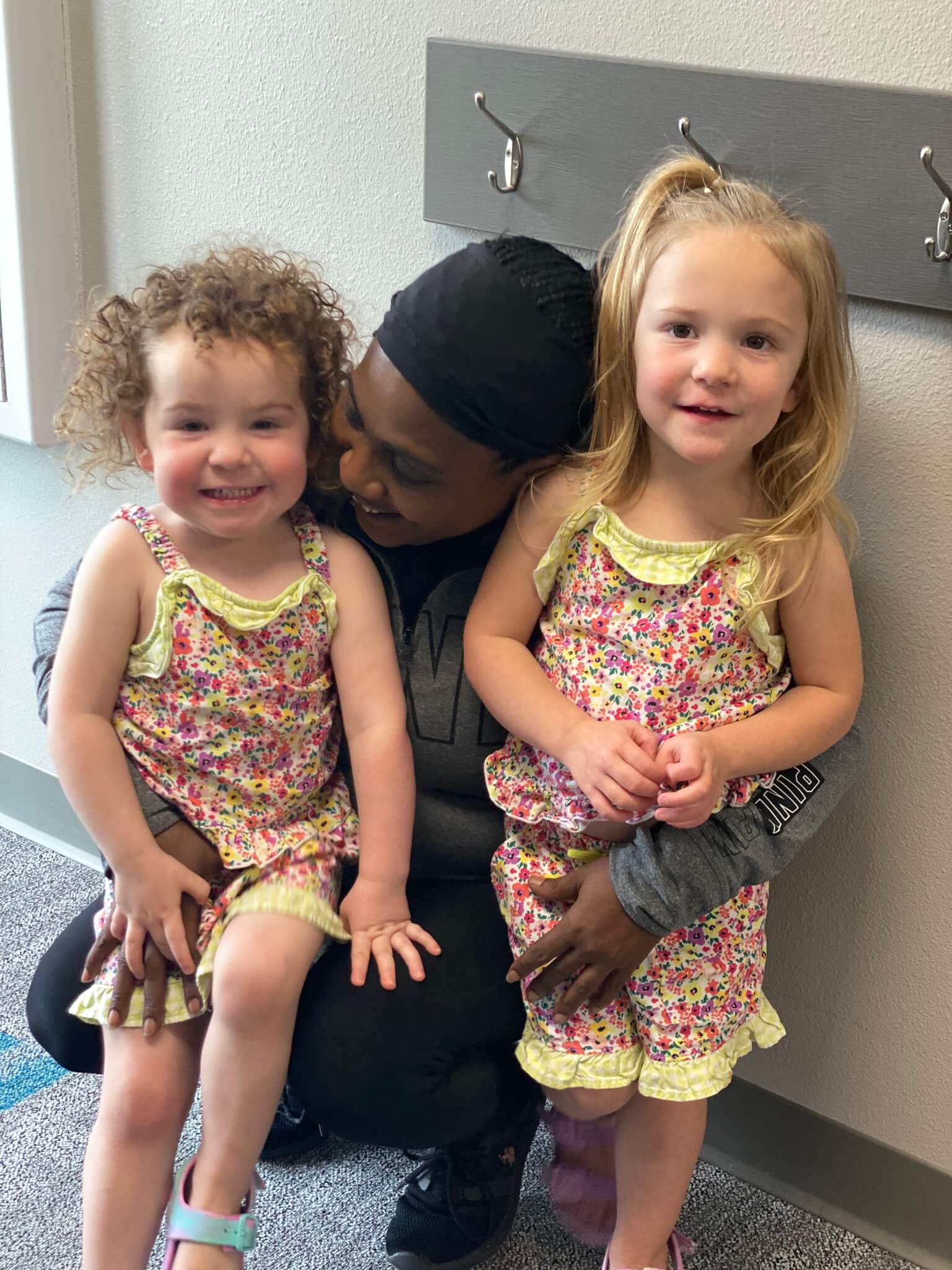 It Takes a Village Childcare employee bent down hugging twin girls