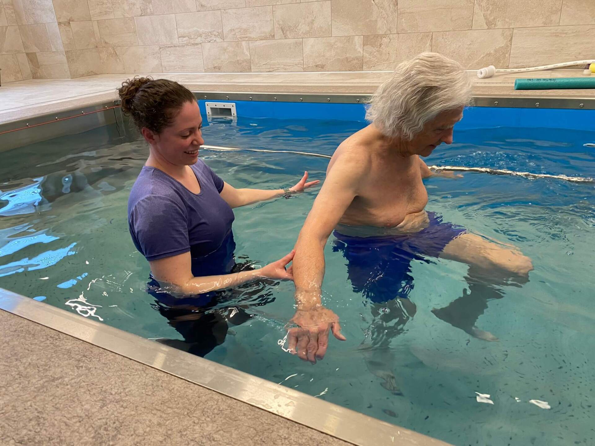 active senior man walking with physical therapist in the newly installed hydro pool