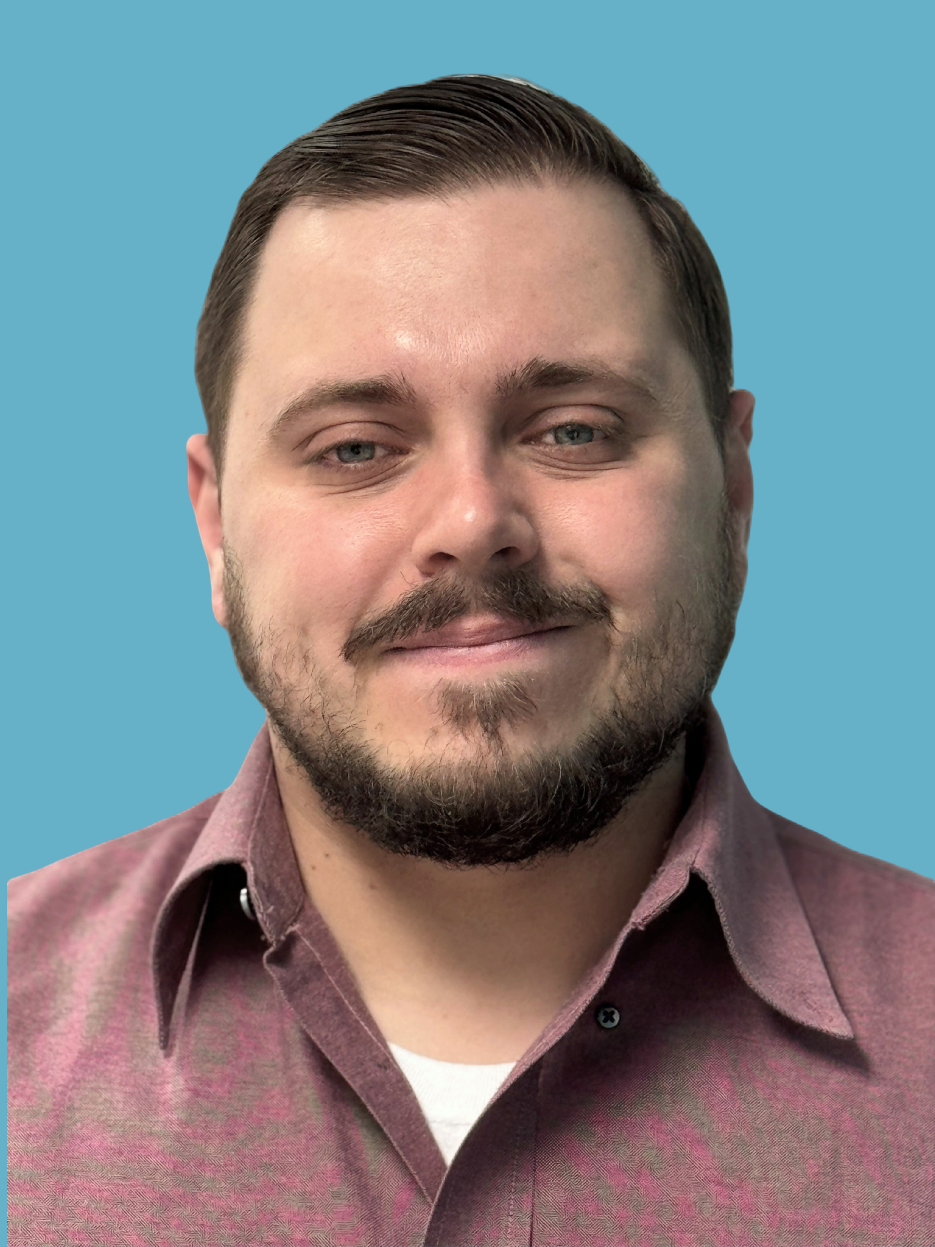 A white man with dark brown hair and beard/mustache against a turquoise color background