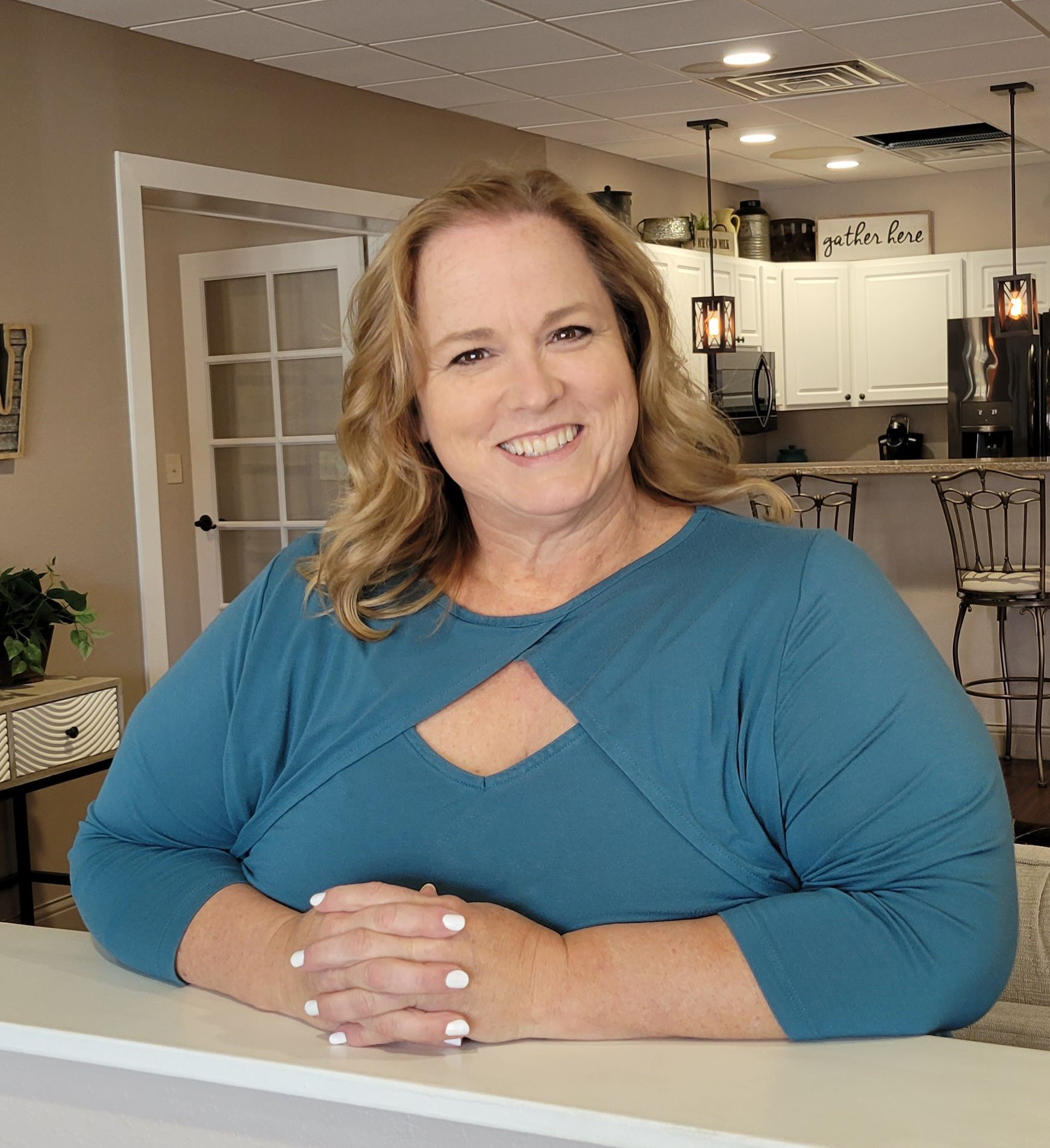 A white woman with medium long brown highlighted hair and a bright turquoise top in an office.