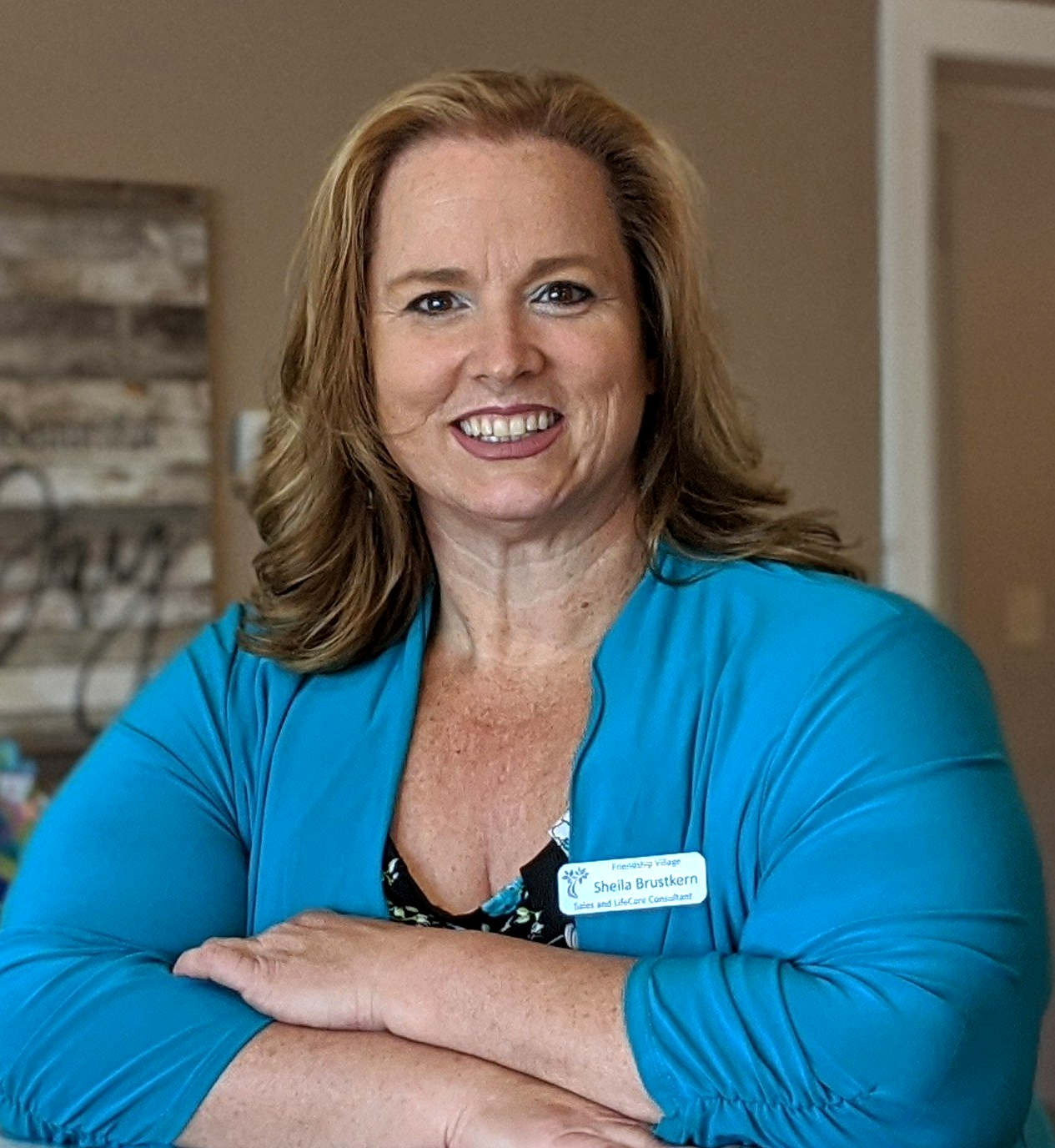 A white woman with medium long brown highlighted hair and a bright turquoise top in an office.