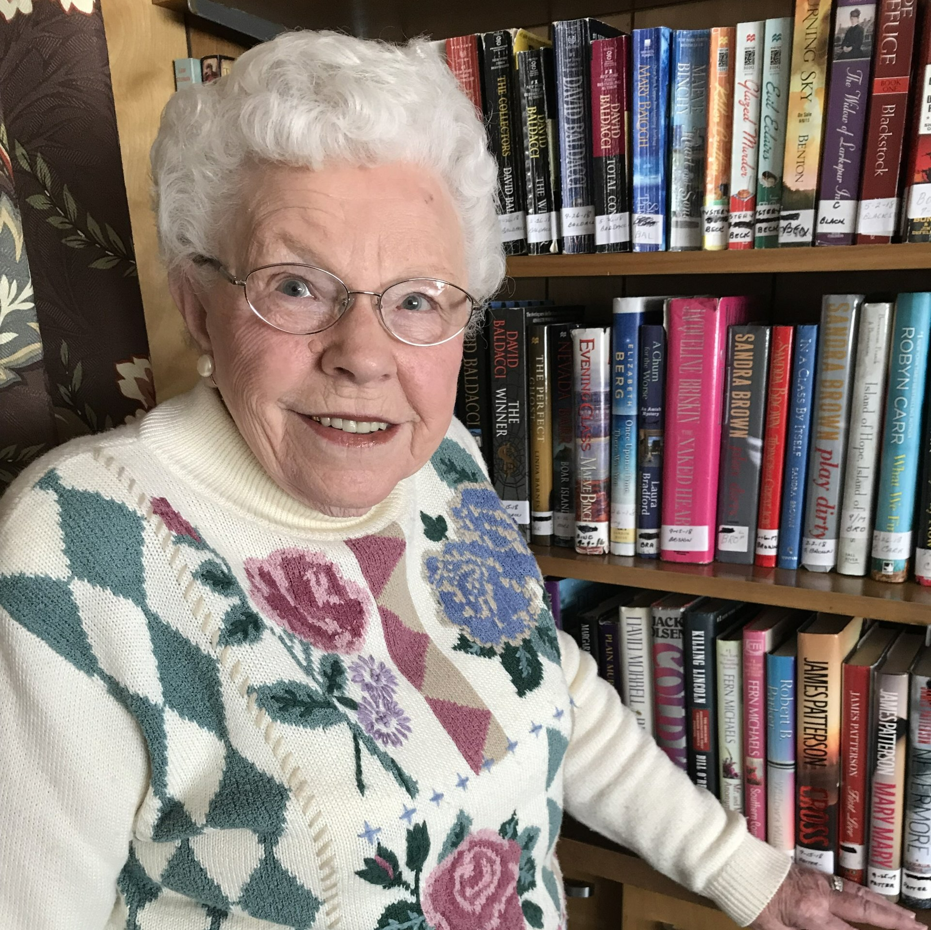 senior lady standing in front of a book shelf full of books