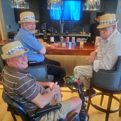 three senior gentlemen sitting at the pub chatting and watching the Kentucky Derby with hats on