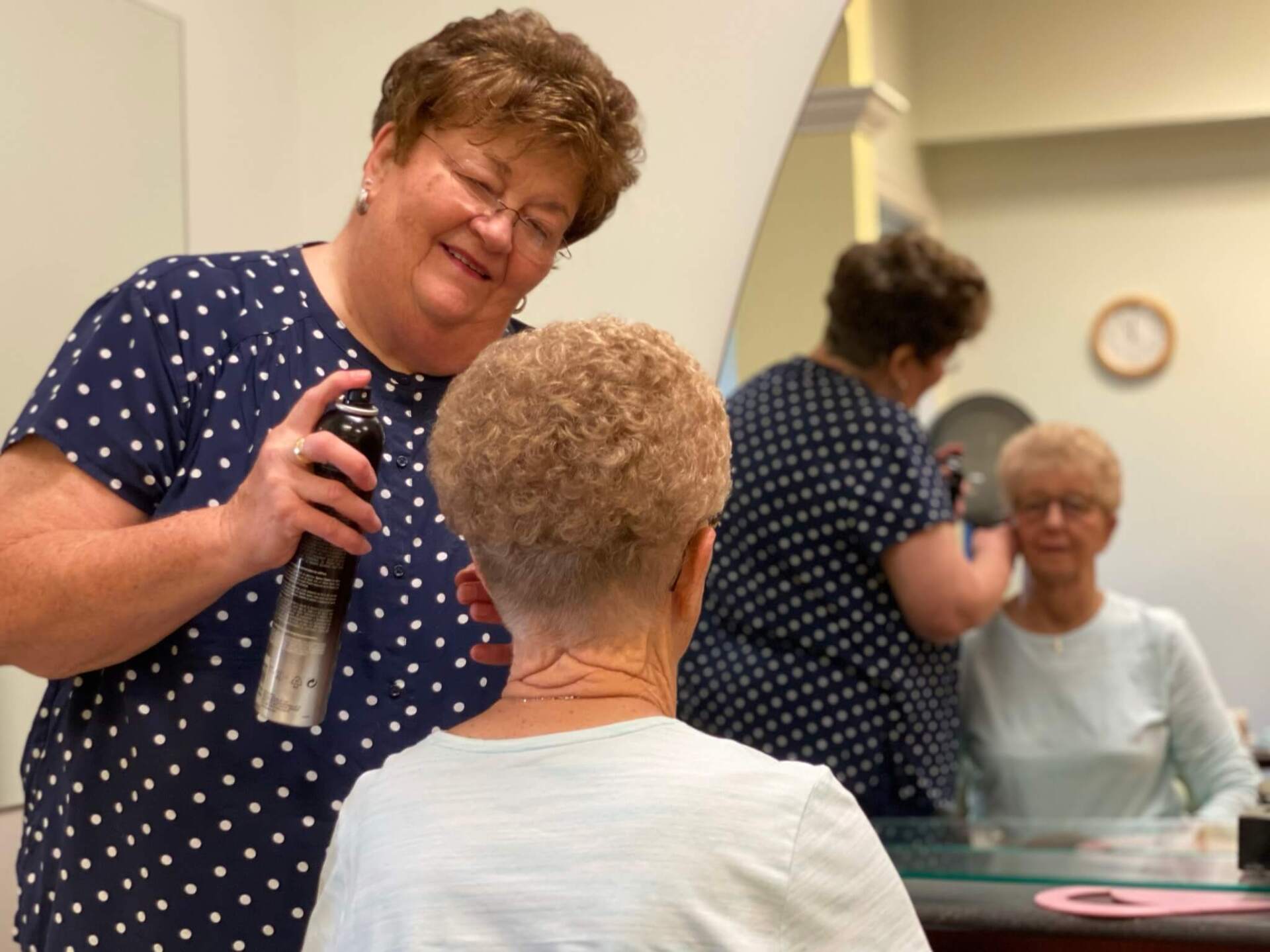 Beautician hair spraying a residents hair while she looks in the mirror