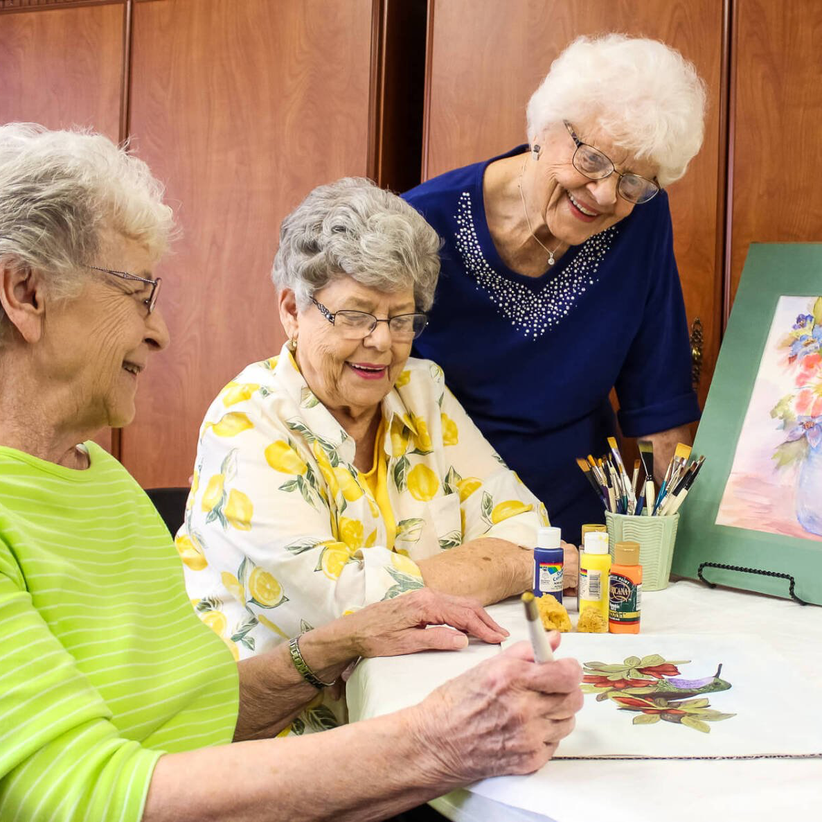 ladies painting a mural of flowers together in the Village Place craft room