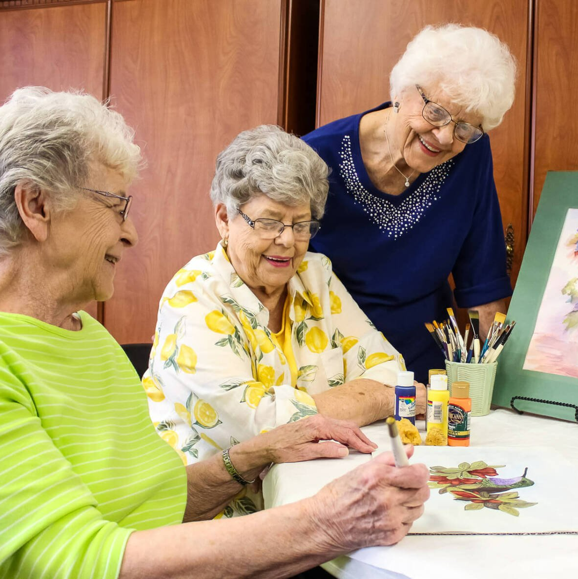 ladies painting a mural of flowers together in the Village Place craft room