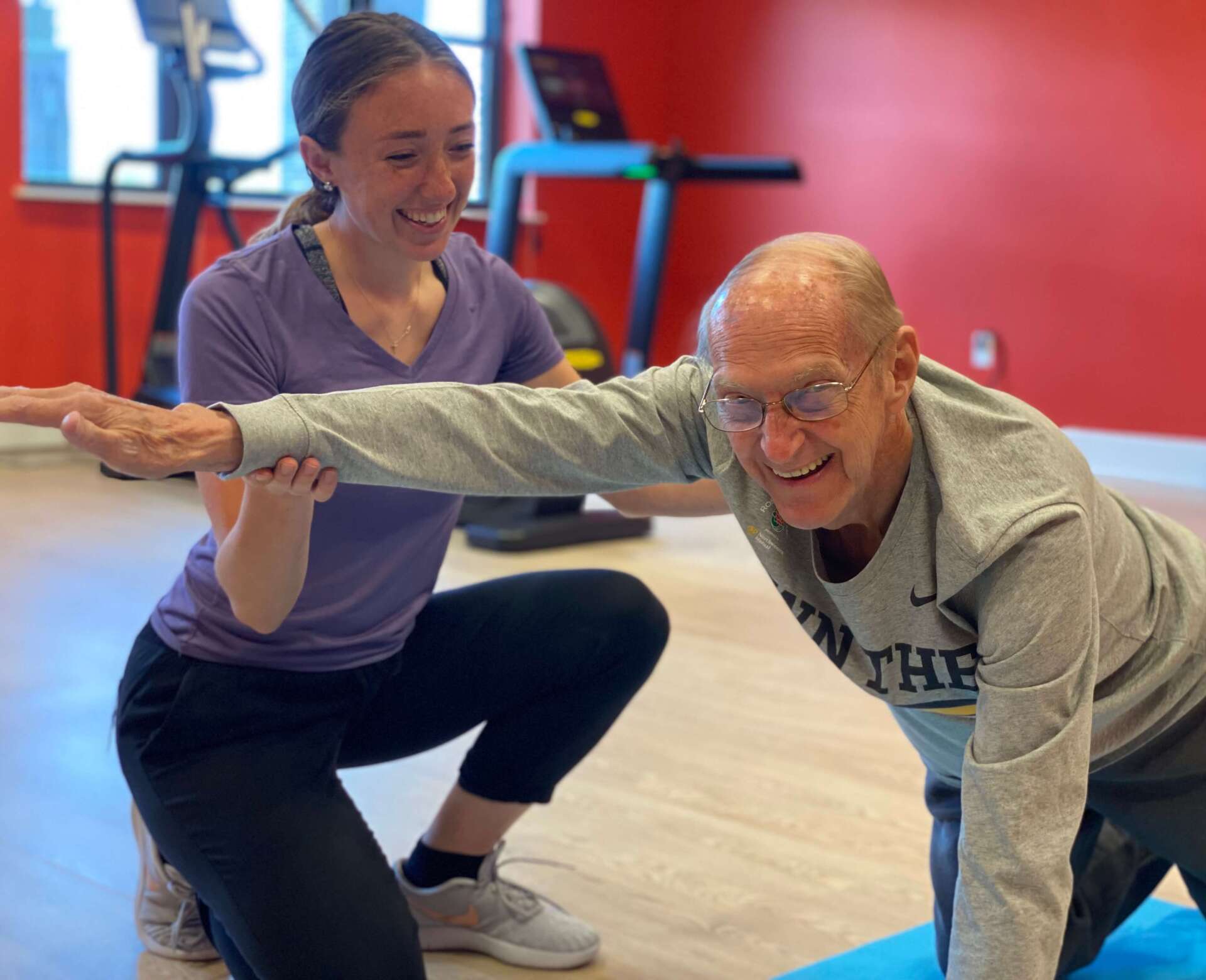 personal trainer working alongside older man stretching his arm while on the ground
