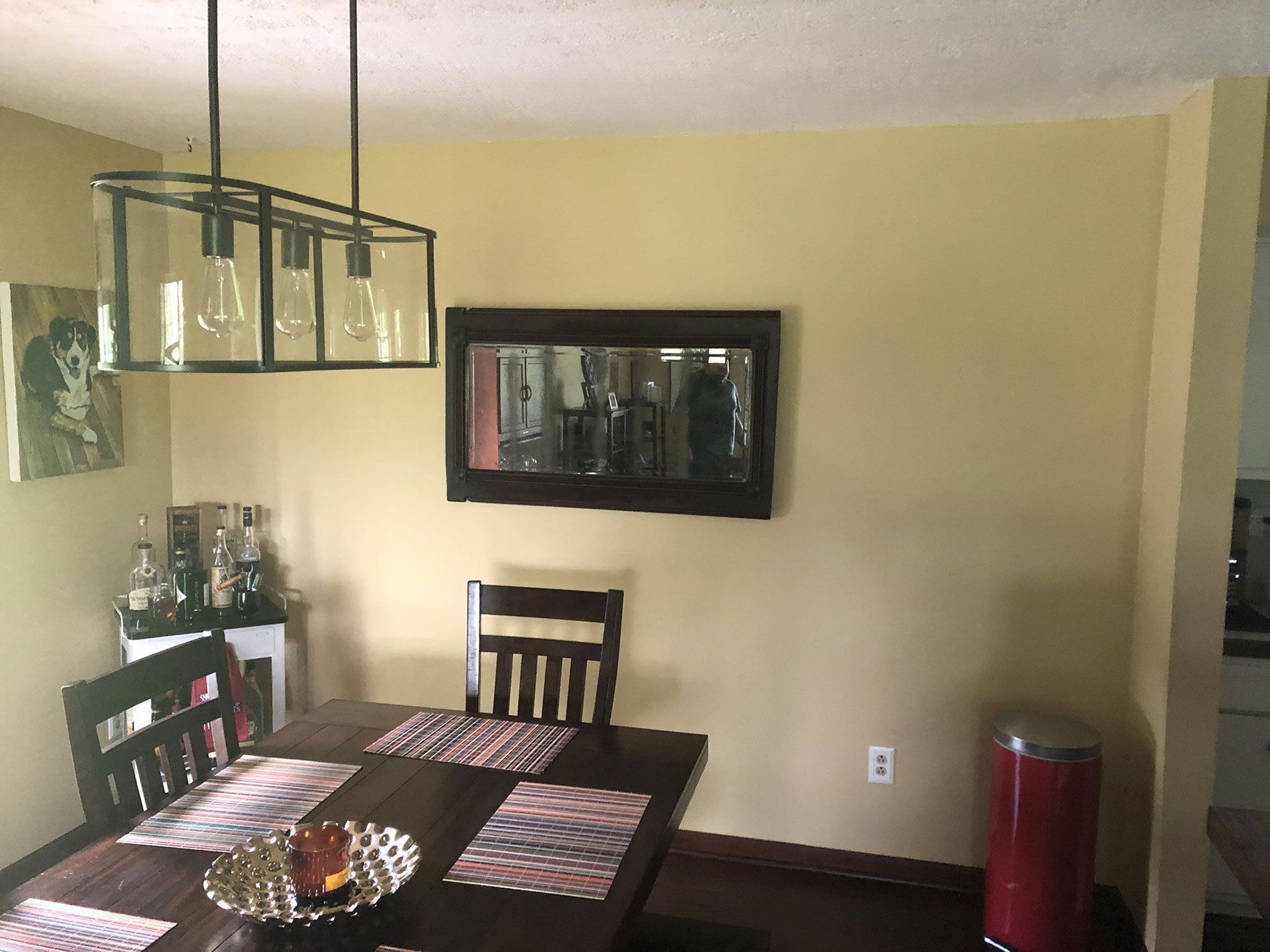 A dining room with a table and chairs and a mirror on the wall.