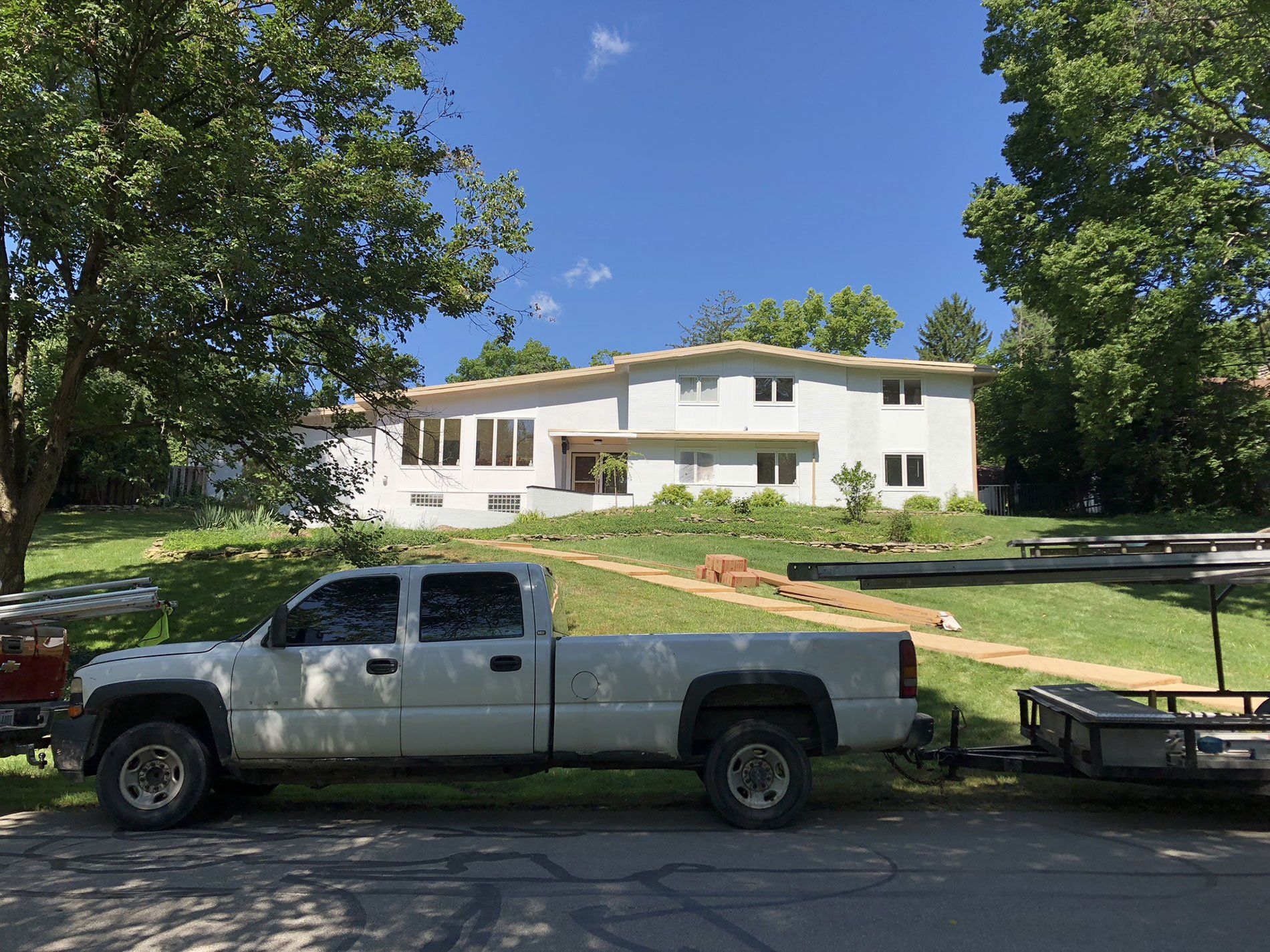 A white truck is parked in front of a large white house.