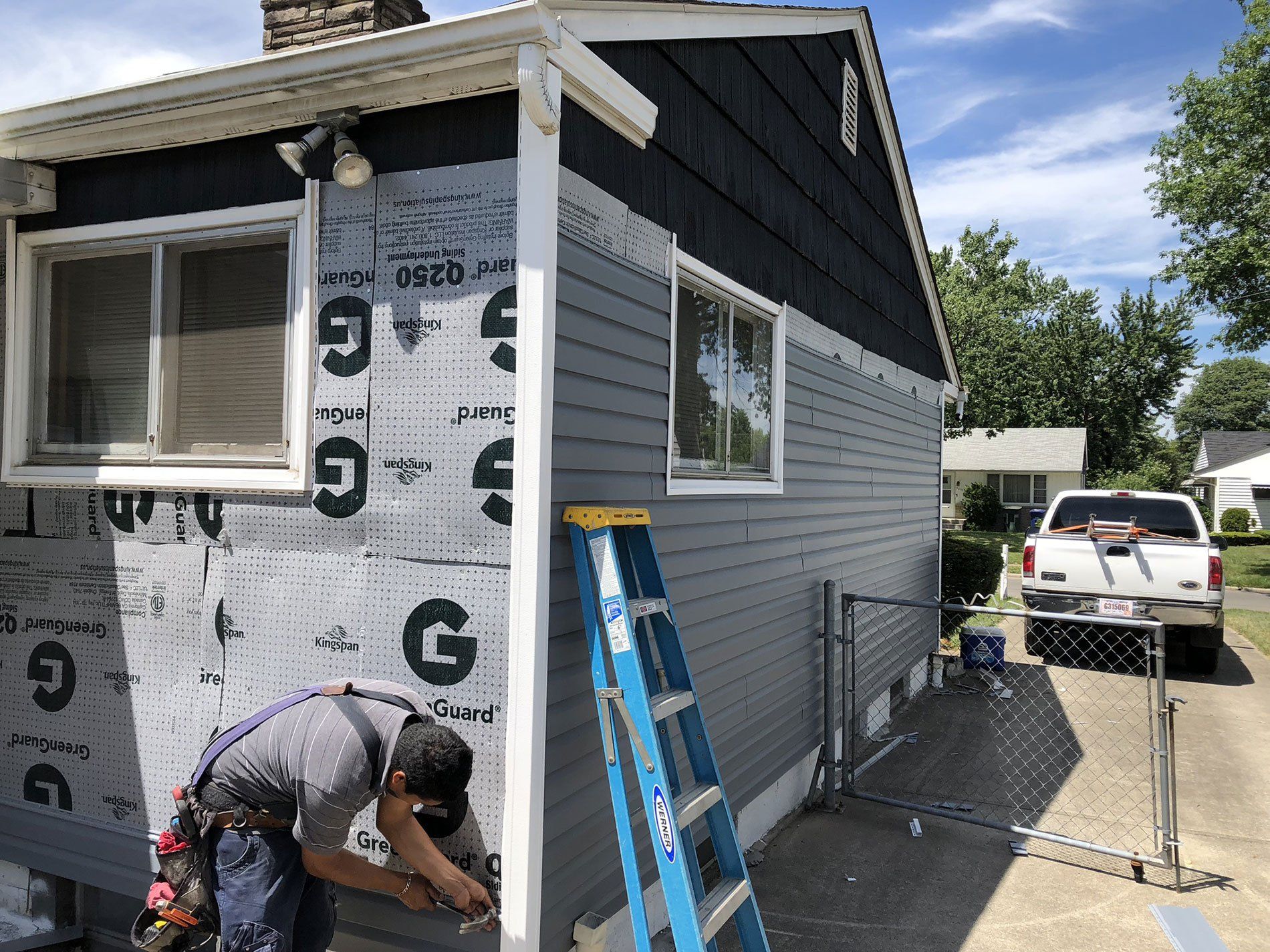 A man is working on the side of a house with a ladder.