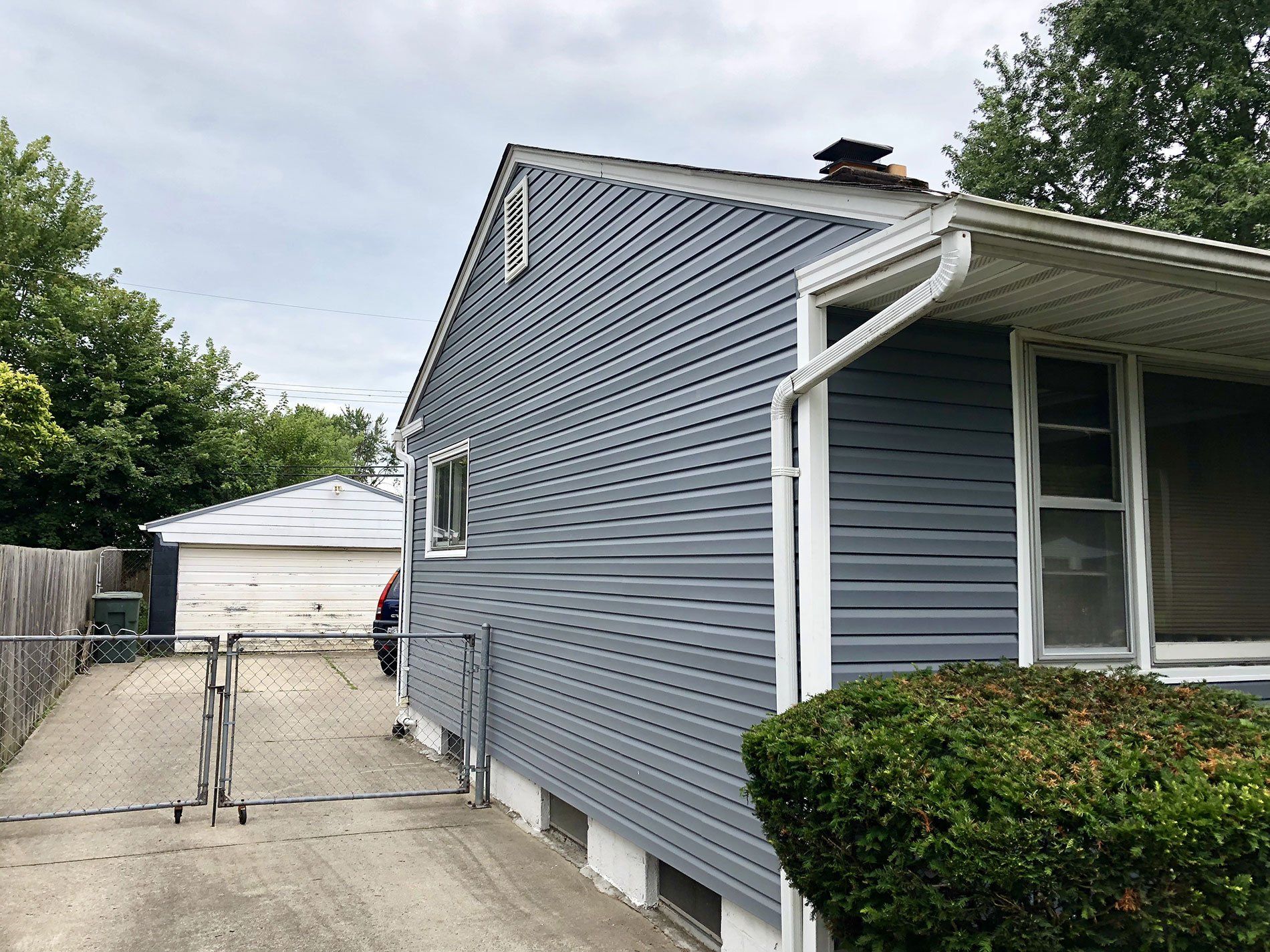 A blue house with white siding and a driveway leading to it.
