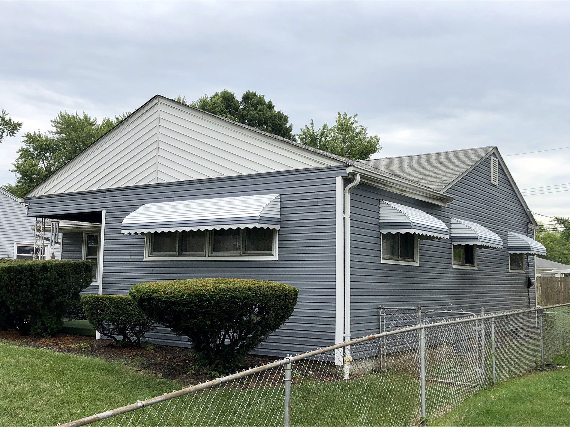 A small house with a fence and awnings on the windows.