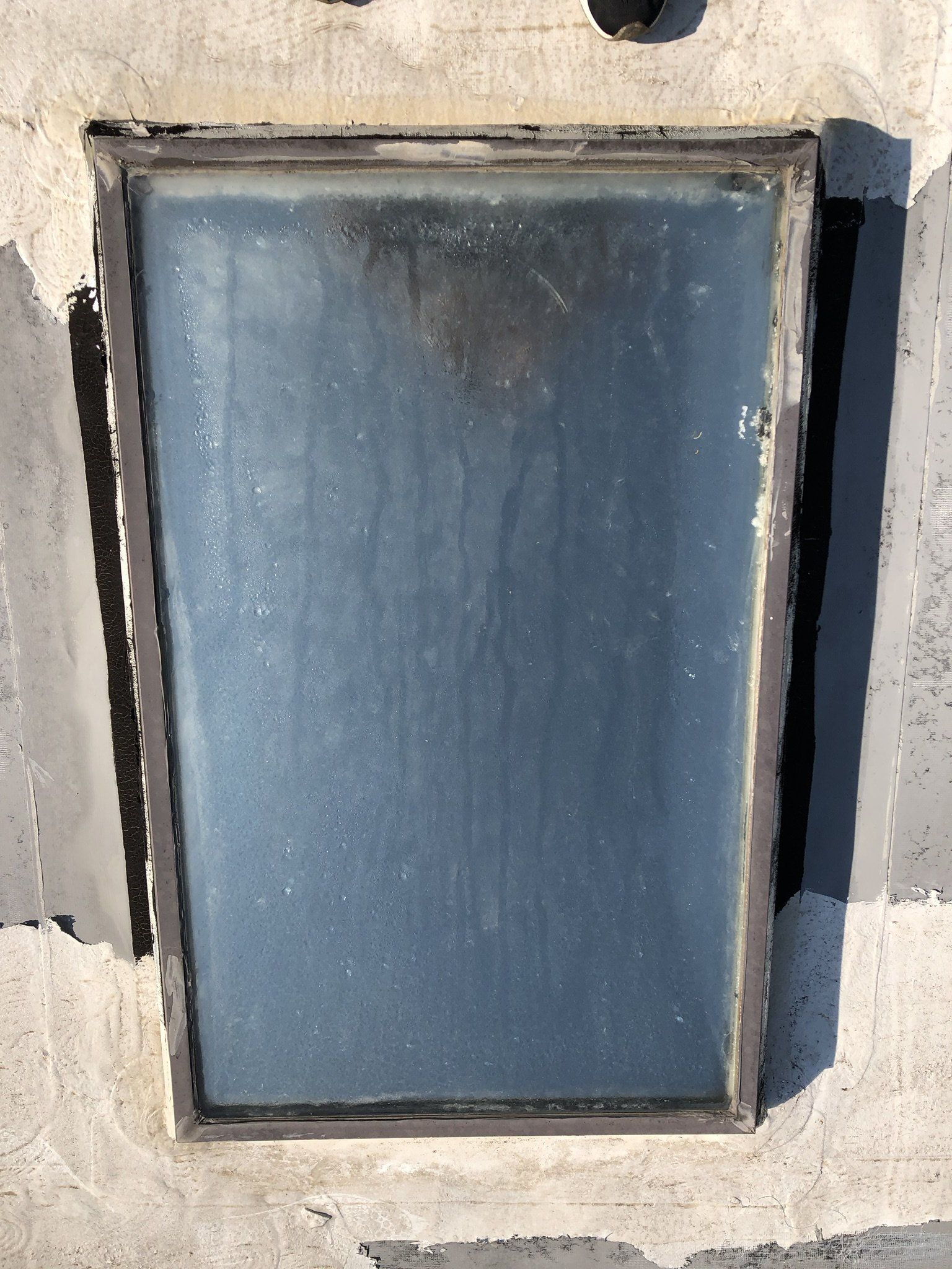 A window with a metal frame is sitting on a concrete wall.