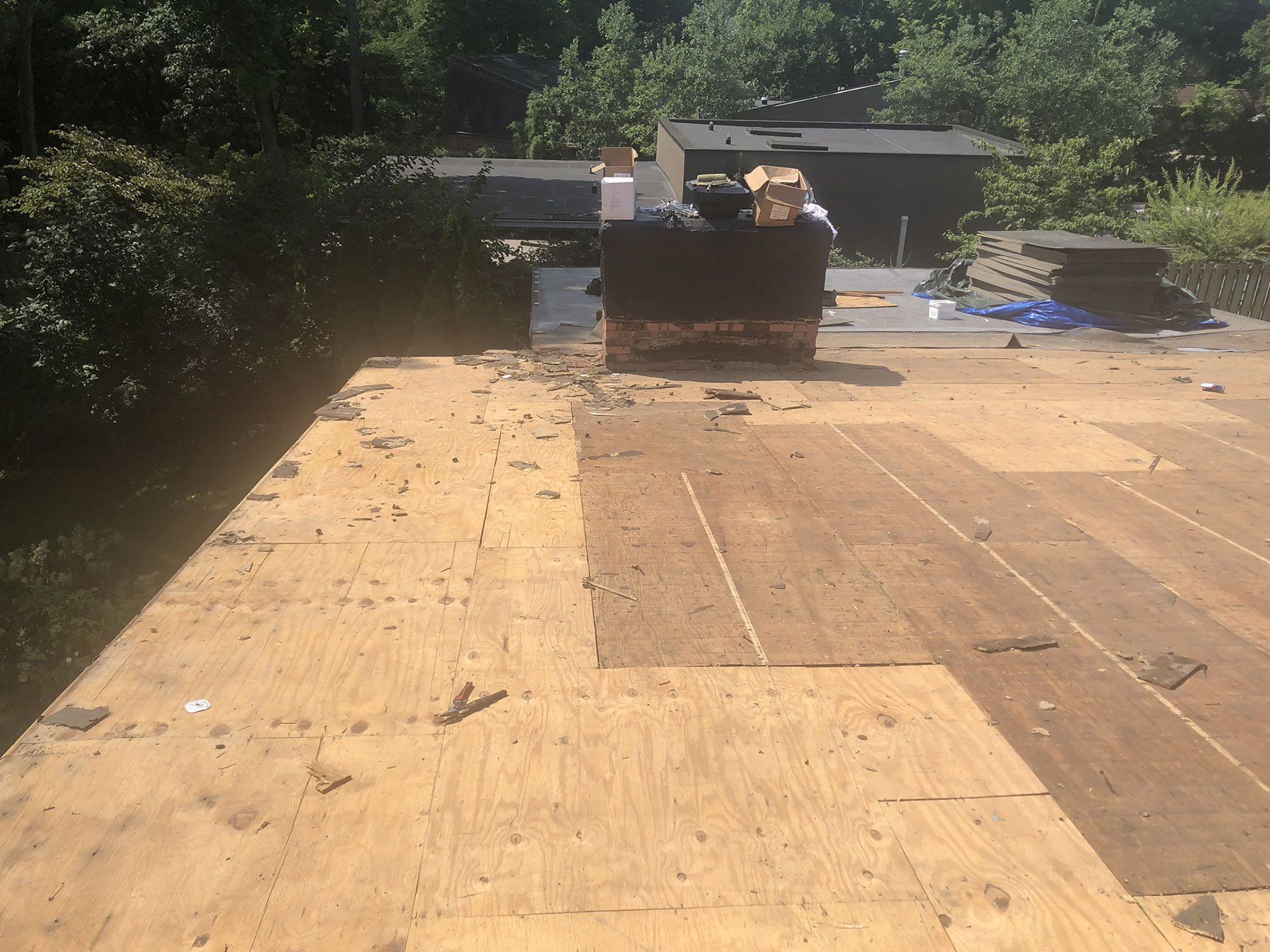 A roof with a lot of plywood on it and a chimney in the background.