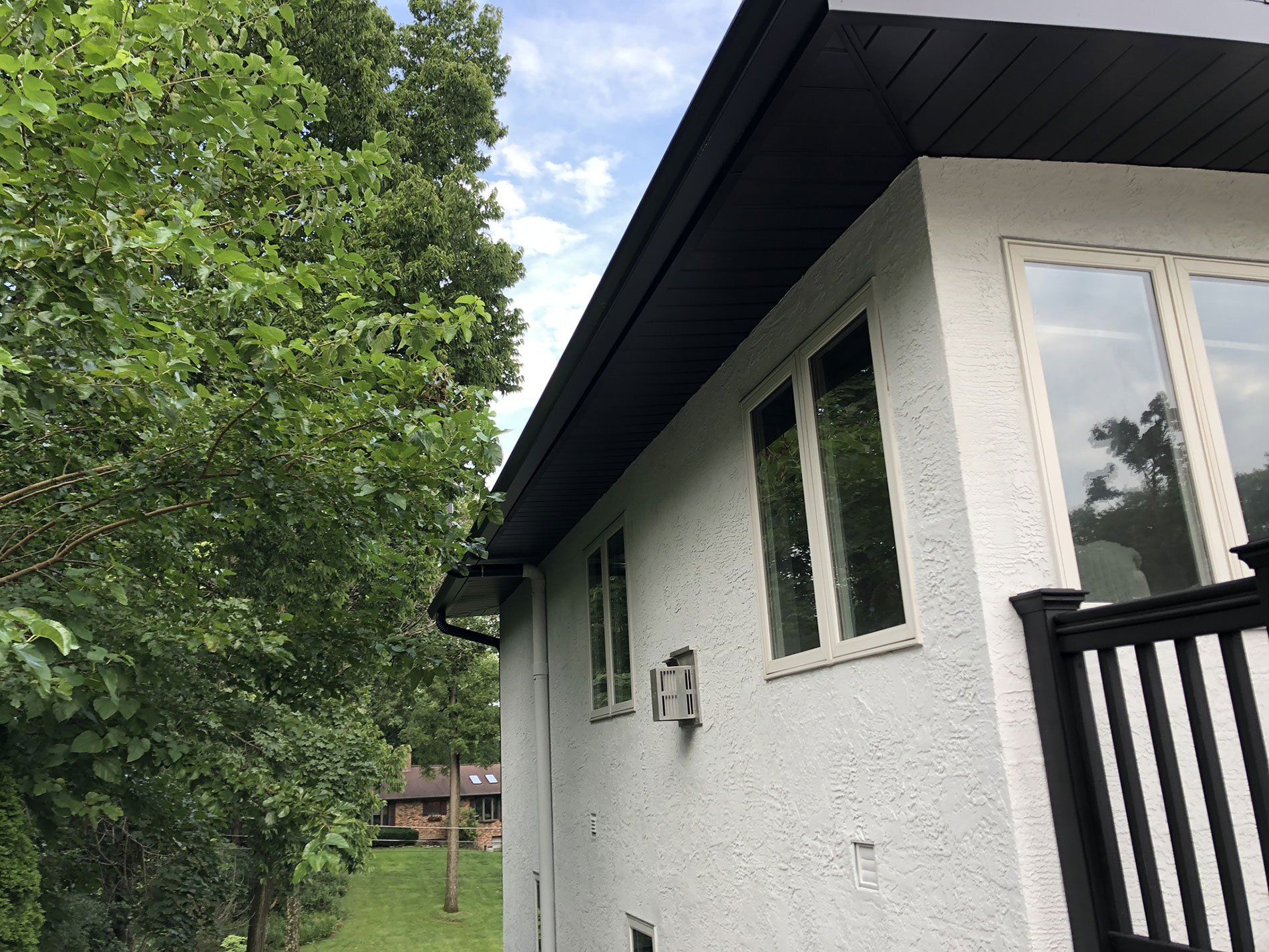 A white house with a black gutter and a balcony surrounded by trees.