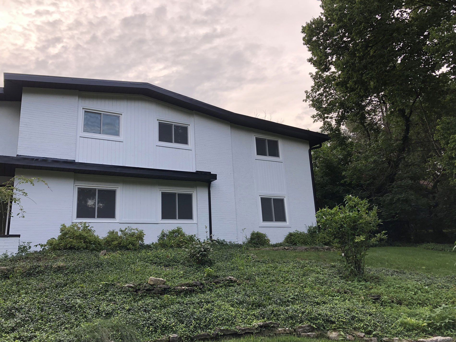 A white house with a black roof is surrounded by trees and grass.