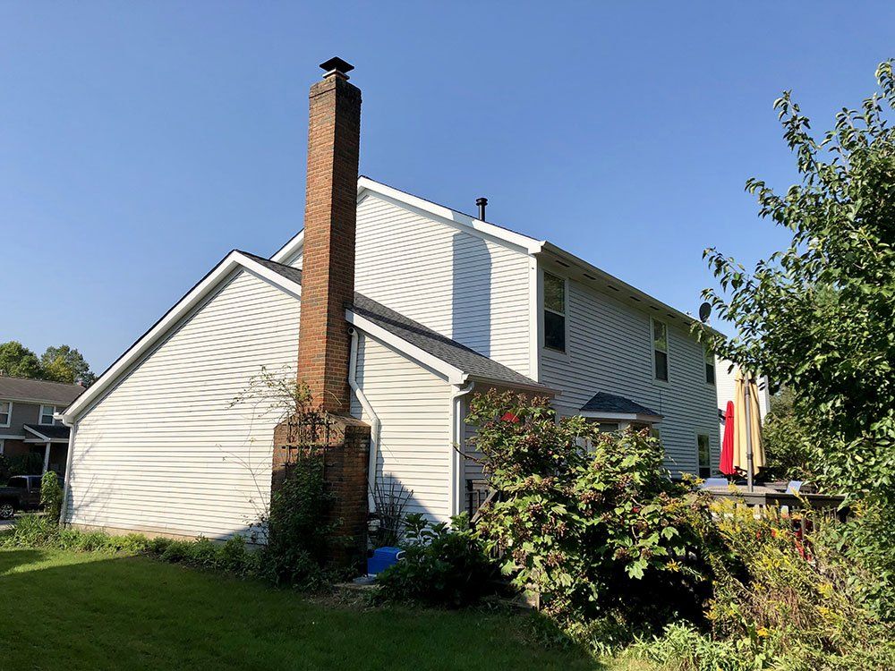 A white house with a brick chimney in the backyard.
