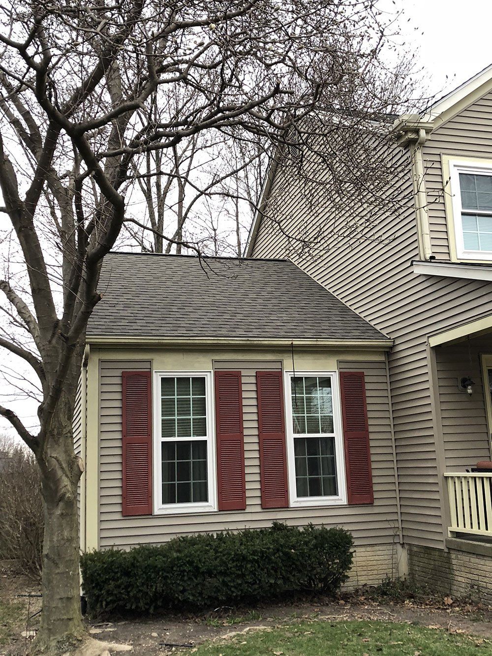 A house with red shutters on the windows and a tree in front of it.