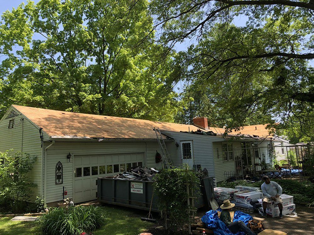 A house with a roof that is being repaired and a dumpster in front of it.
