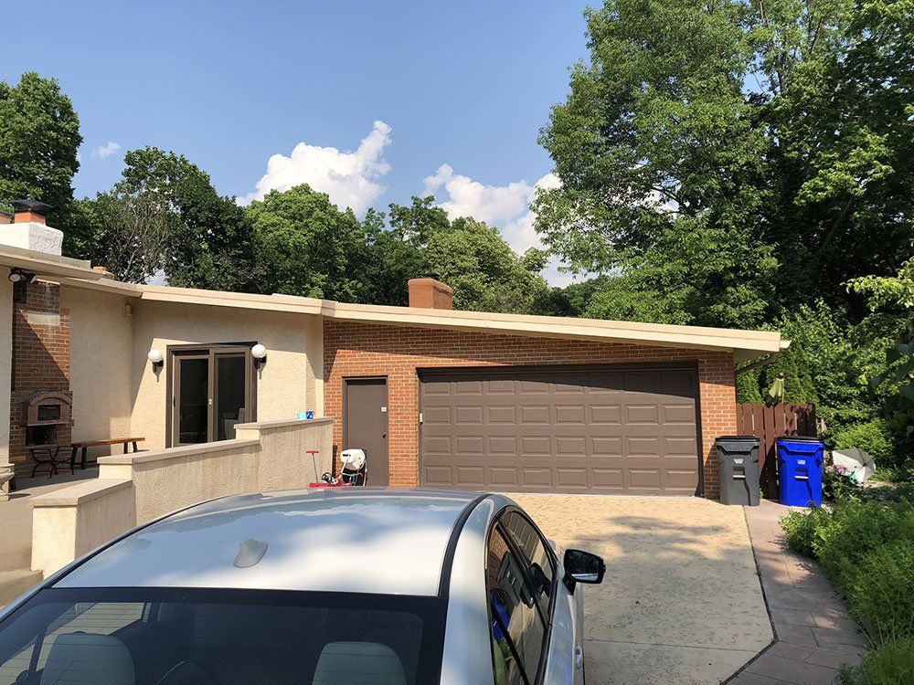 A car is parked in front of a house with a garage door.