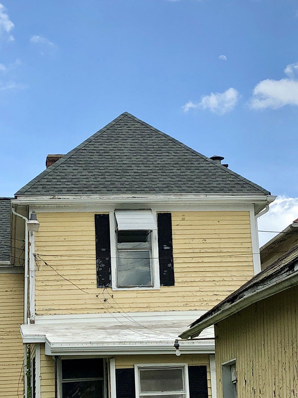 A yellow house with a gray roof and black shutters.