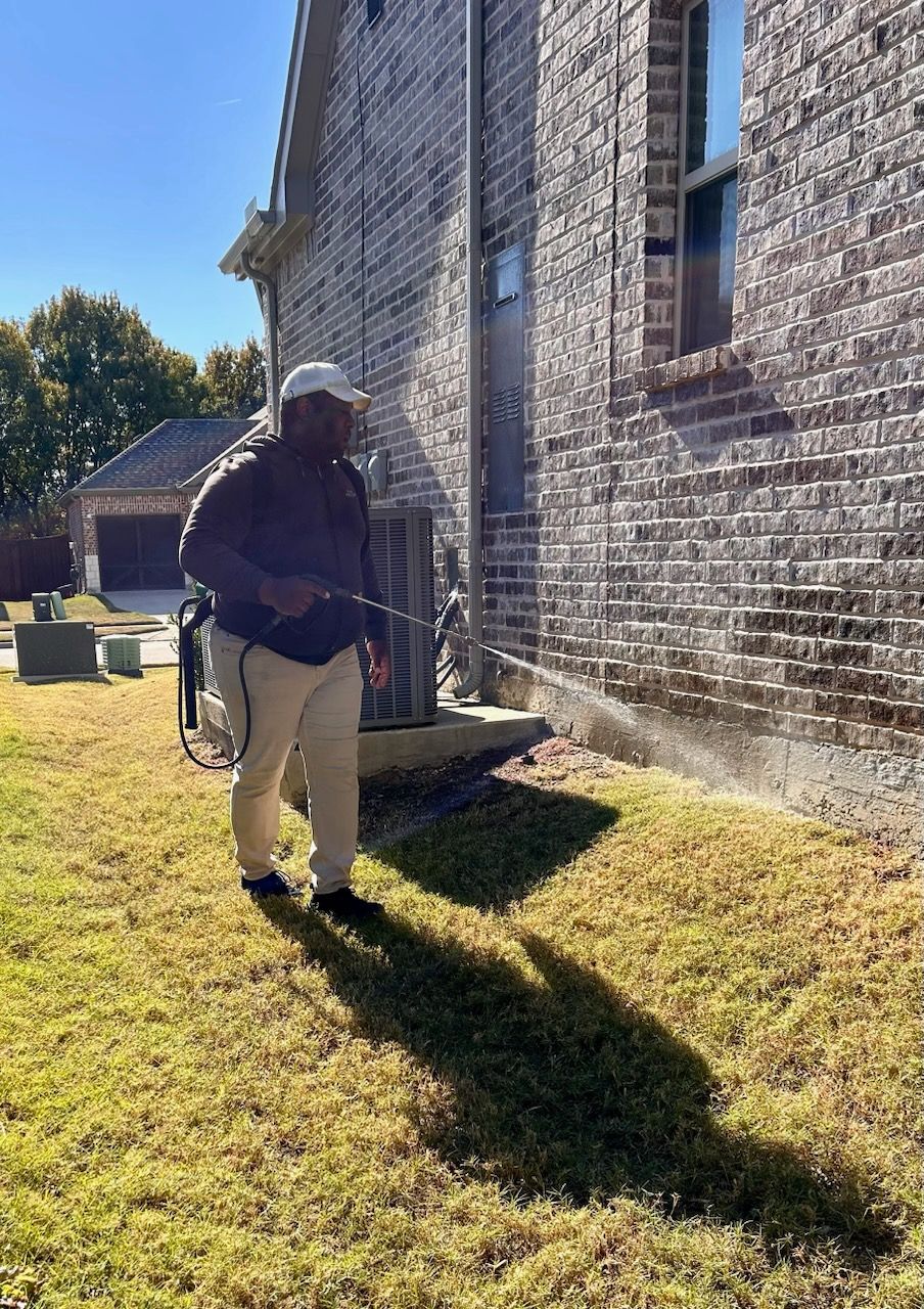 A technician is treating pest on the side of a brick house.