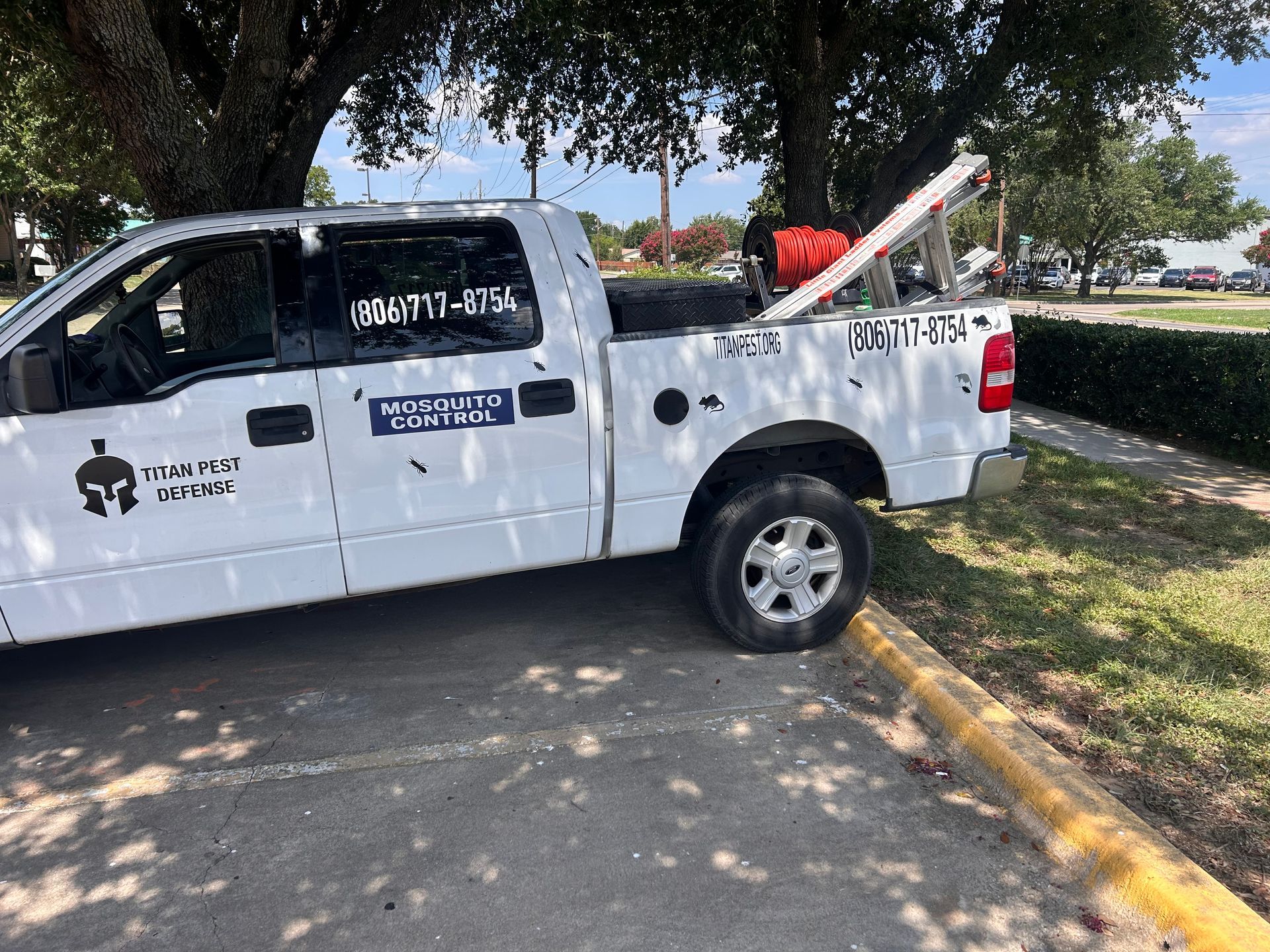 Titan Pest Defense truck is parked in a parking lot next to a tree.