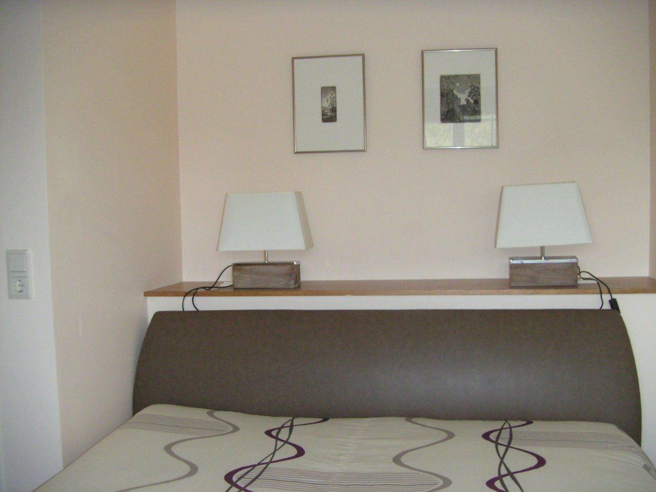 Een slaapkamer met twee lampen en twee schilderijen aan de muur boven het bed