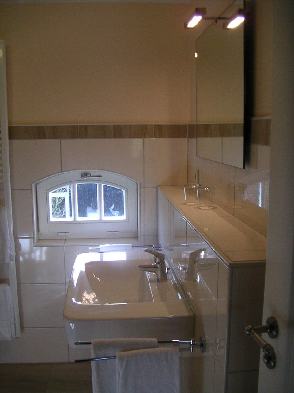 Een badkamer met een wastafel, een spiegel en een raam