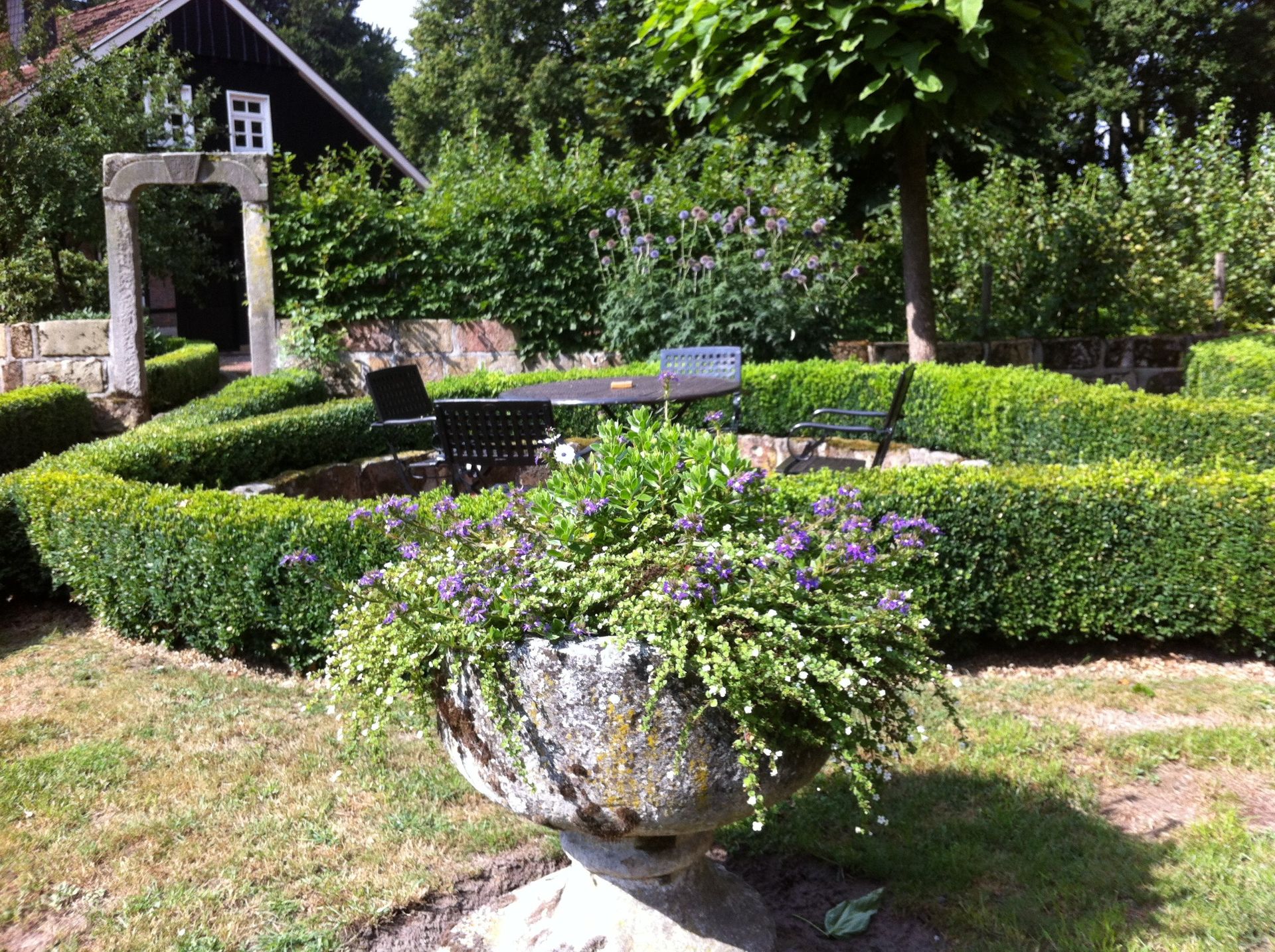 Een stenen urn gevuld met paarse bloemen staat in het midden van een tuin.