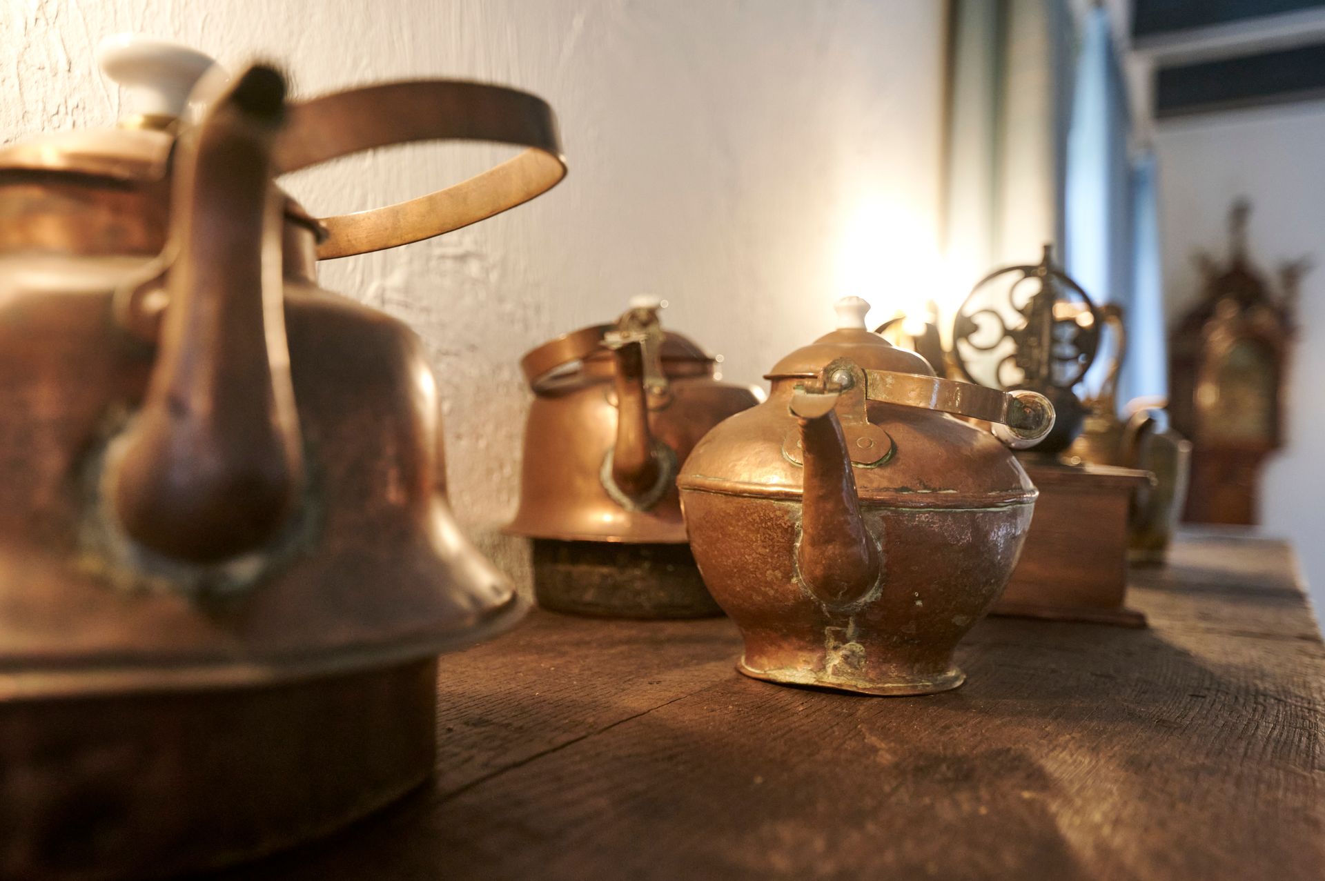 Auf einem Holztisch steht eine Reihe Kupferteekannen.