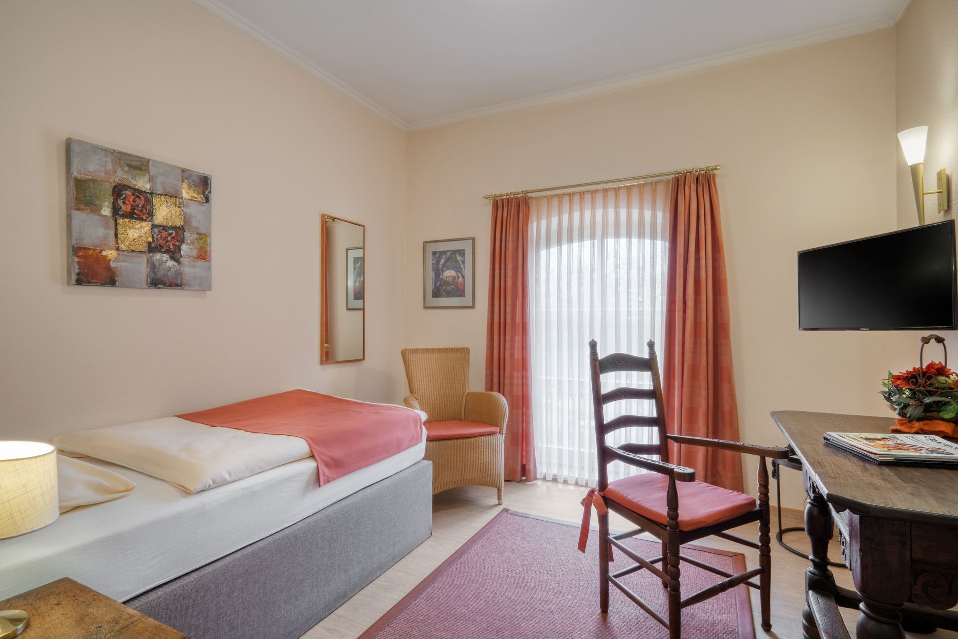 Ein Schlafzimmer mit Einzelbett, Sessel, Schreibtisch und Fernseher.