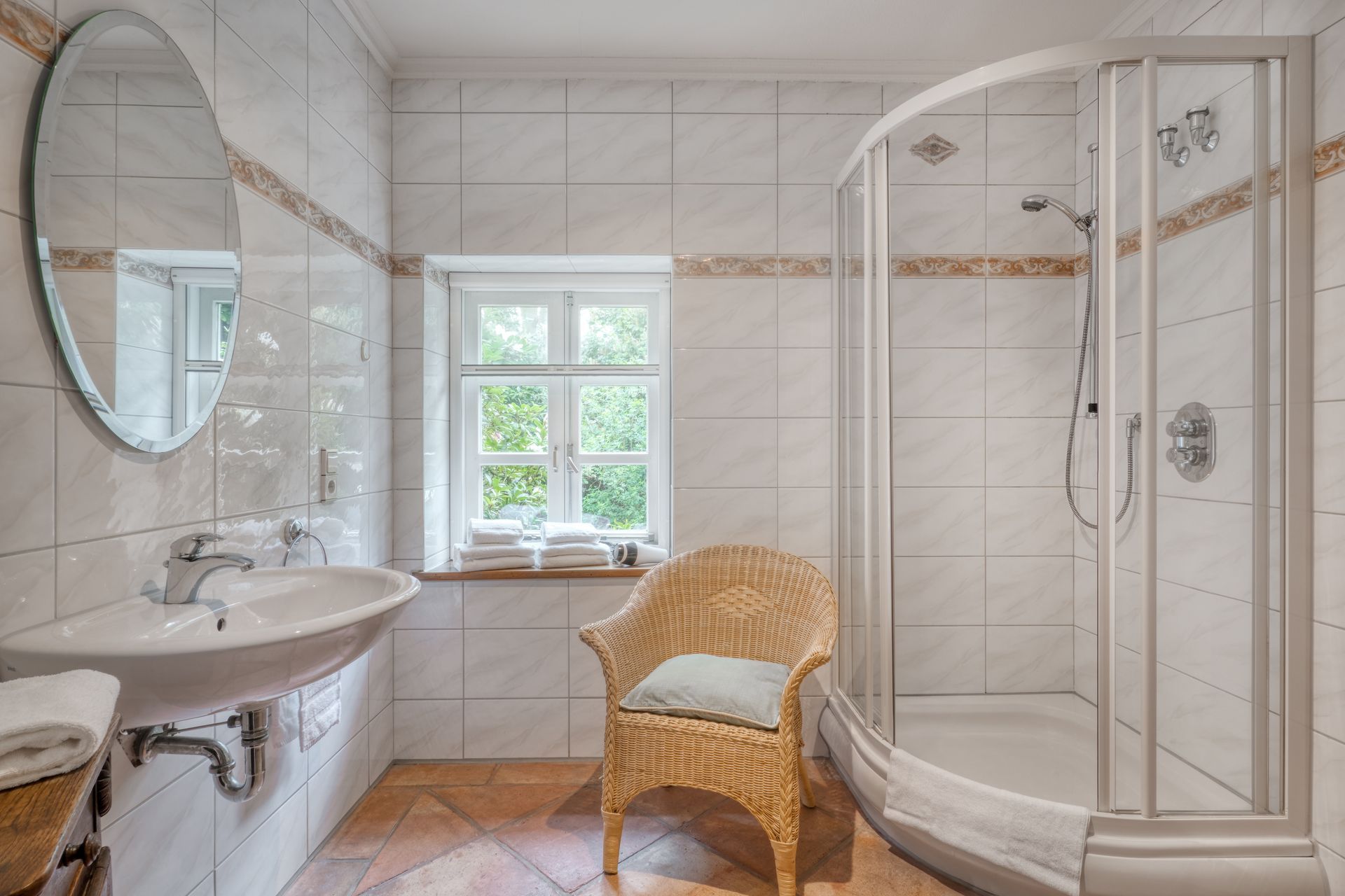 Ein Badezimmer mit Korbstuhl, Waschbecken, Dusche und Spiegel.