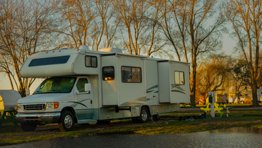 A white recreational vehicle parked on grass among trees during golden hour.