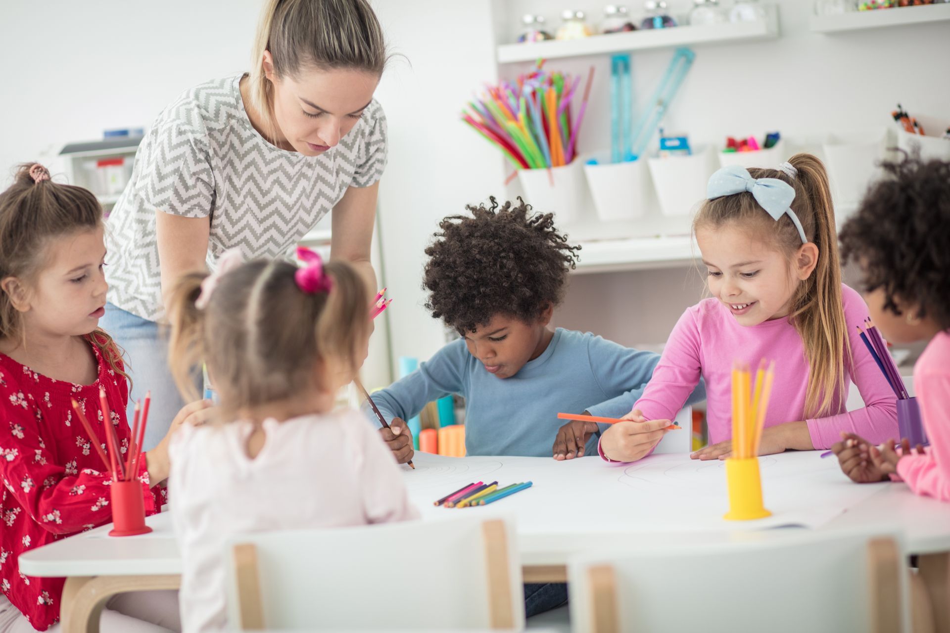 Teacher assisting young children with drawing and writing activities.