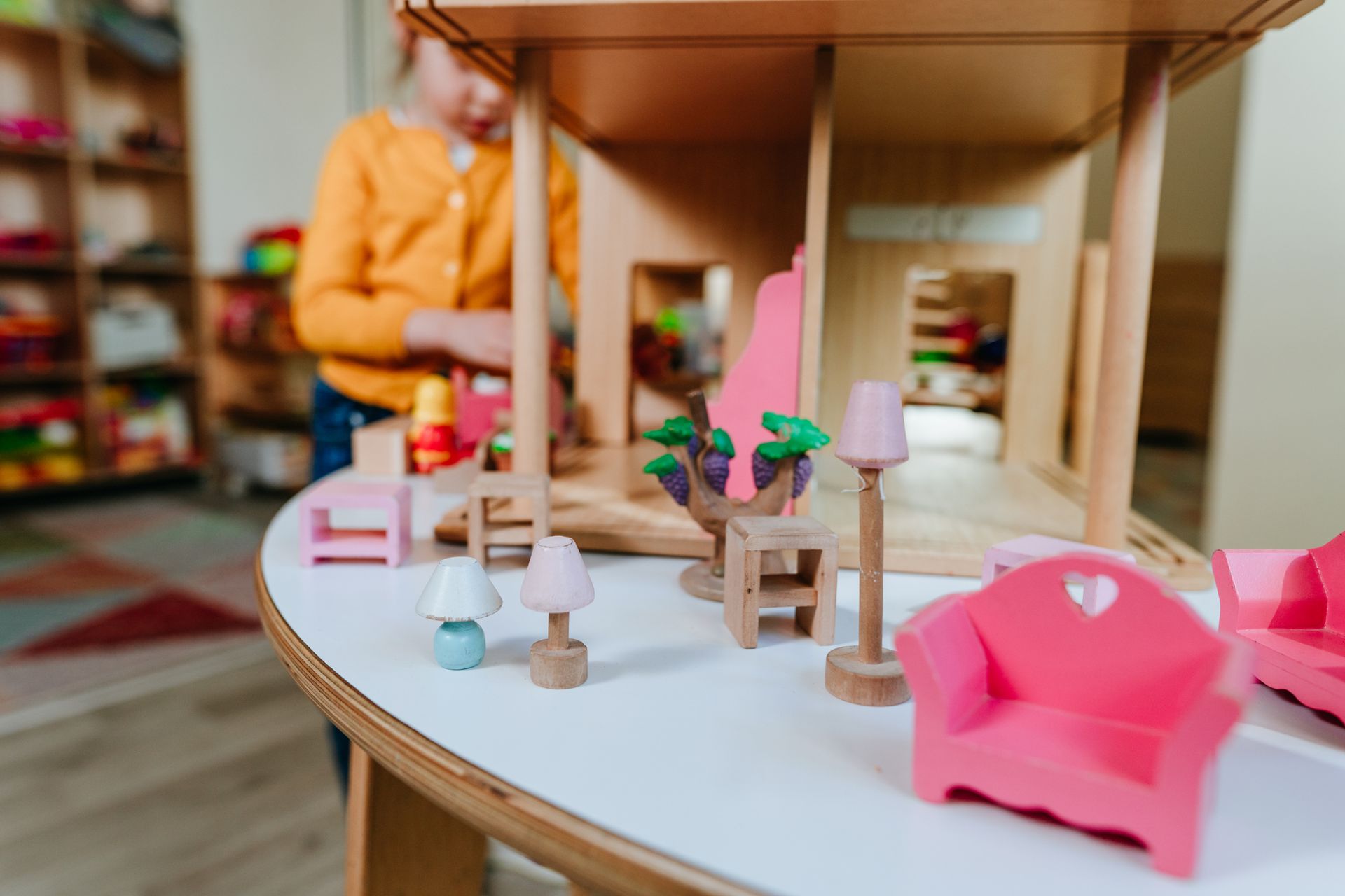 Child playing with dollhouse and miniature furniture.