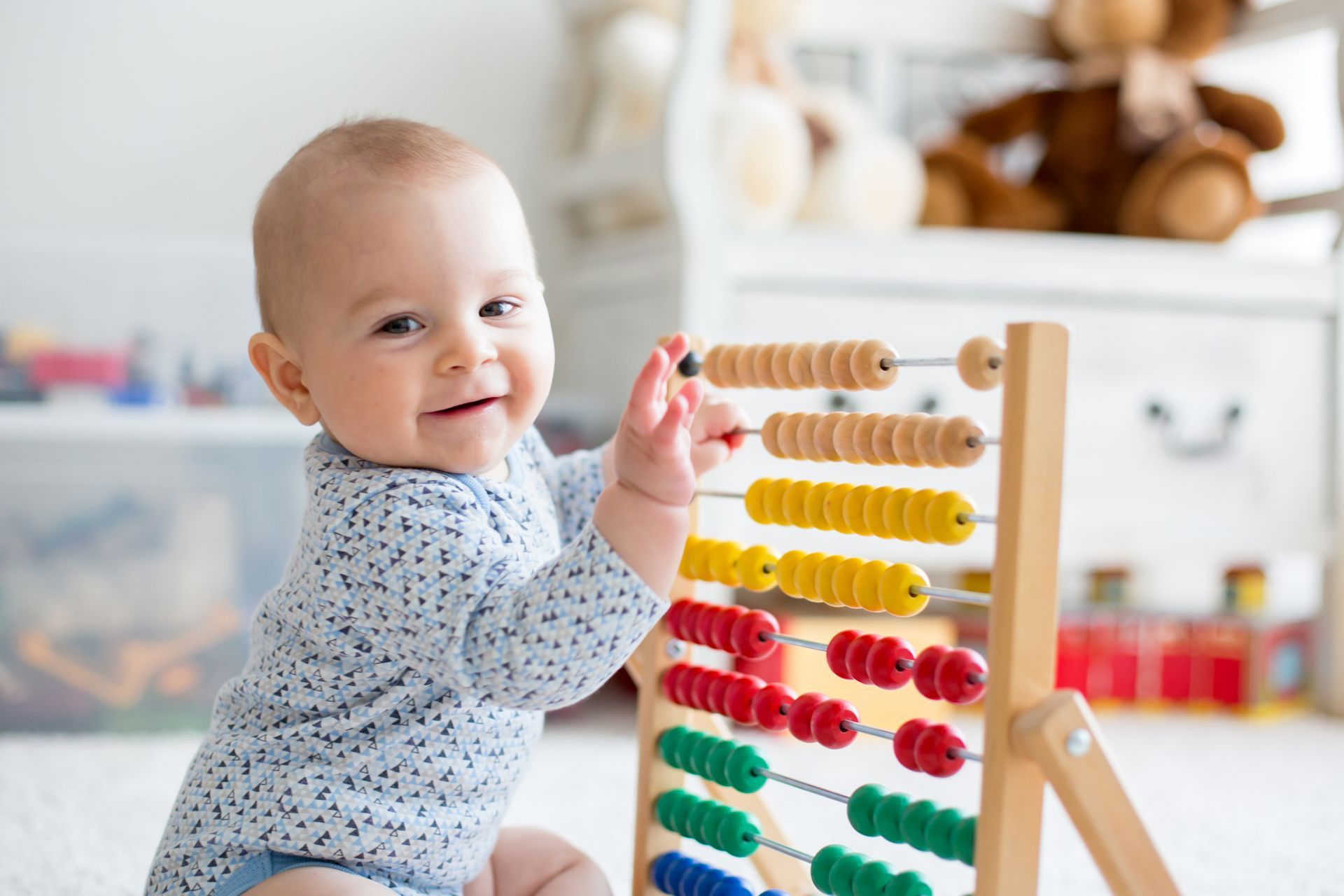 A cute baby, smiling at the camera, plays with a toy with rows of colourful beads.