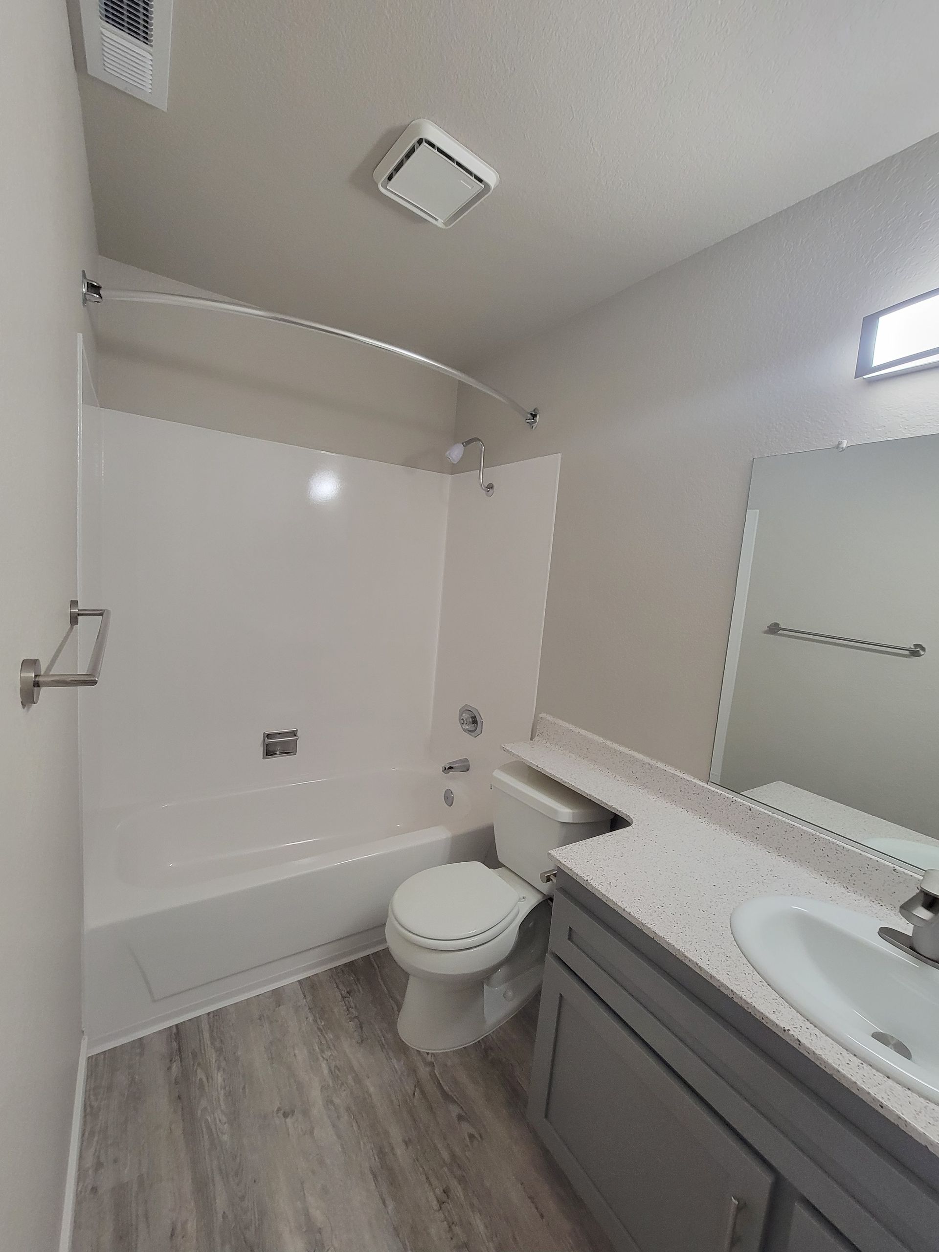 Bathroom with white tub, toilet, gray vanity, and light gray flooring.