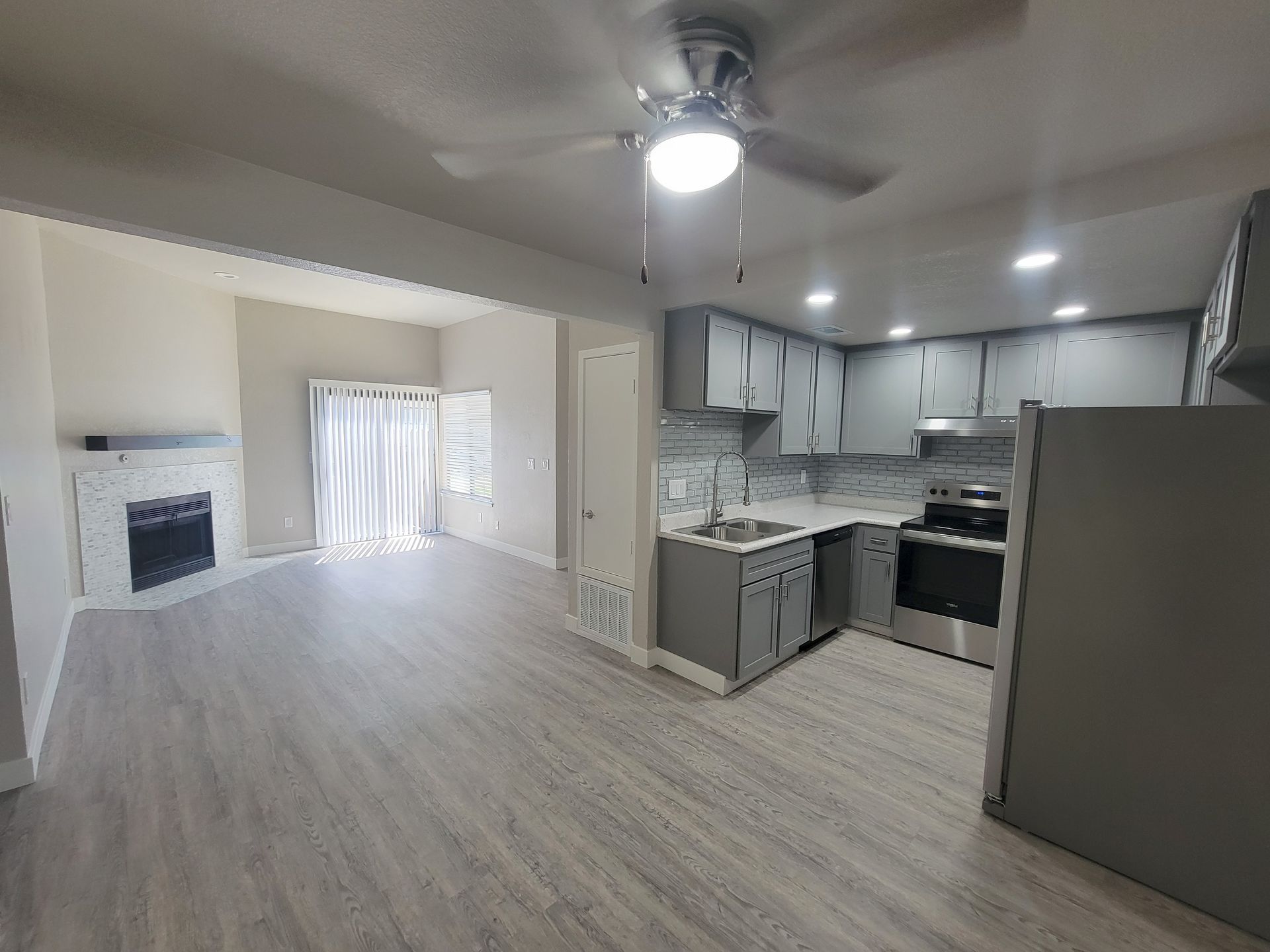 Open-concept living space with kitchen and living room. Gray cabinets, stainless steel appliances, and a fireplace.