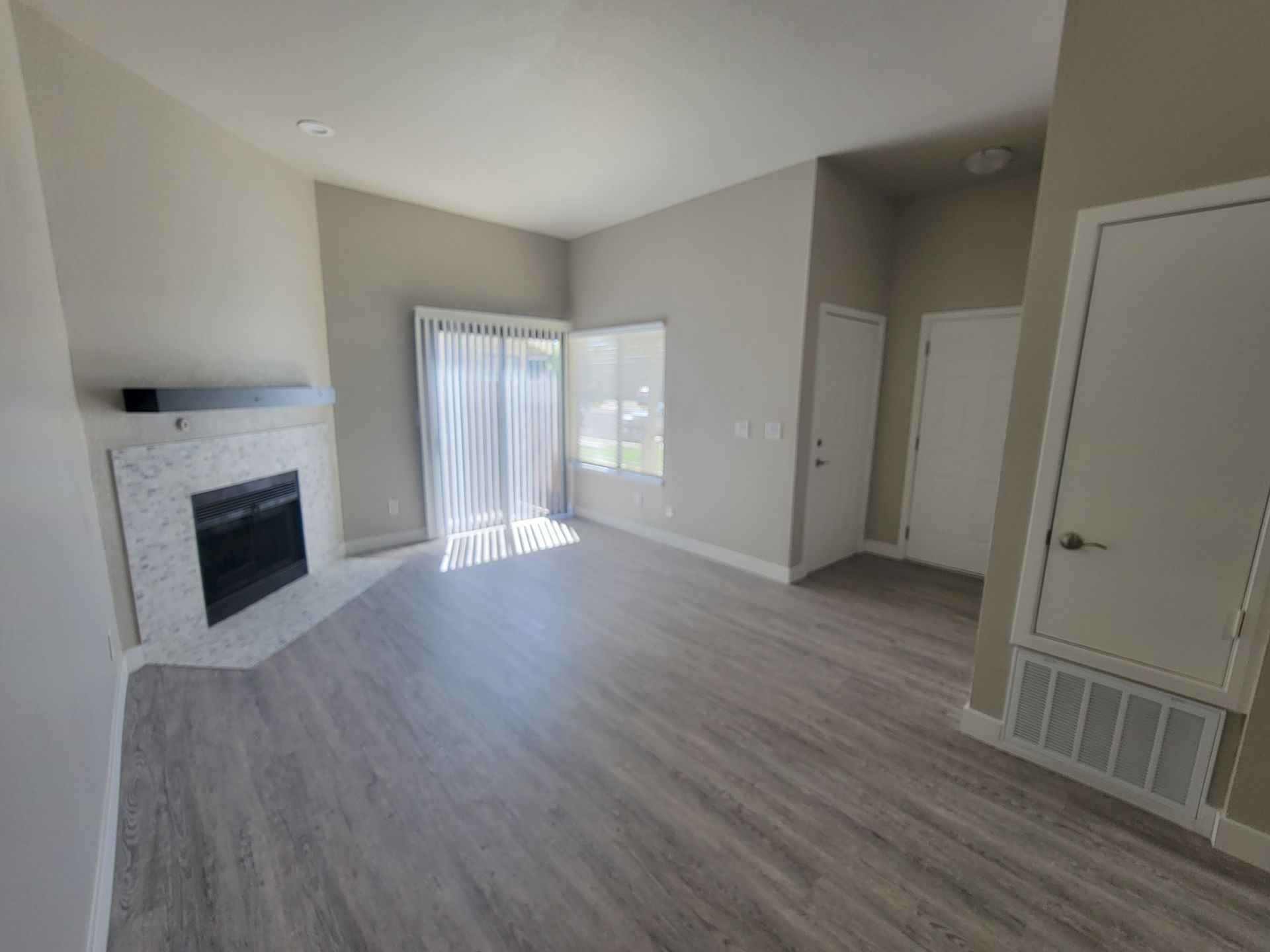Empty living room with fireplace, sliding door, gray walls, and wood-look flooring.