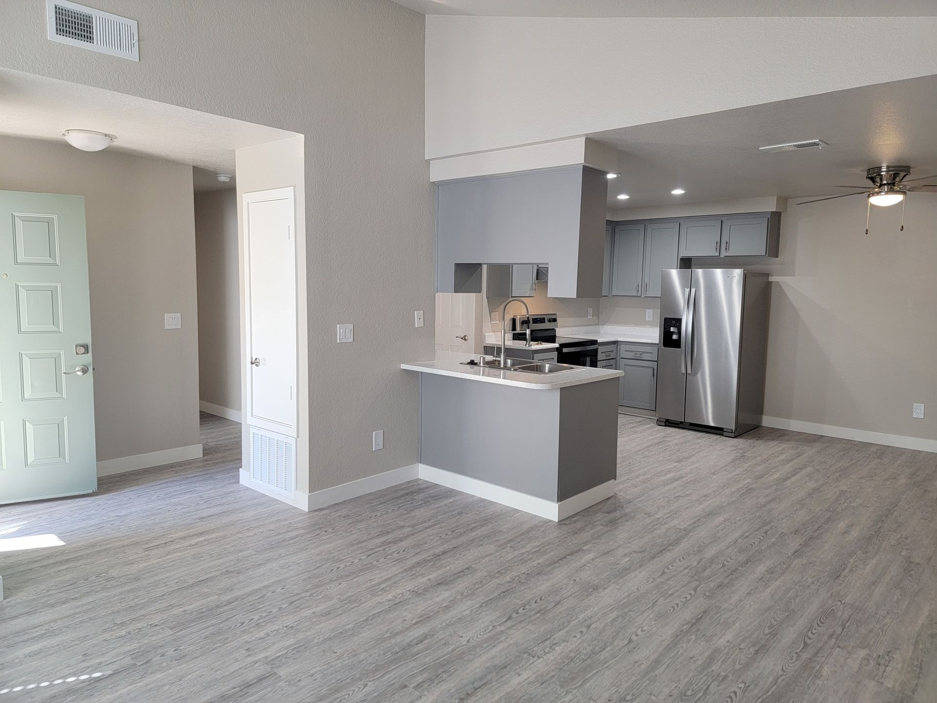 Open-concept kitchen and living area, light gray walls, with a kitchen island and stainless steel refrigerator.