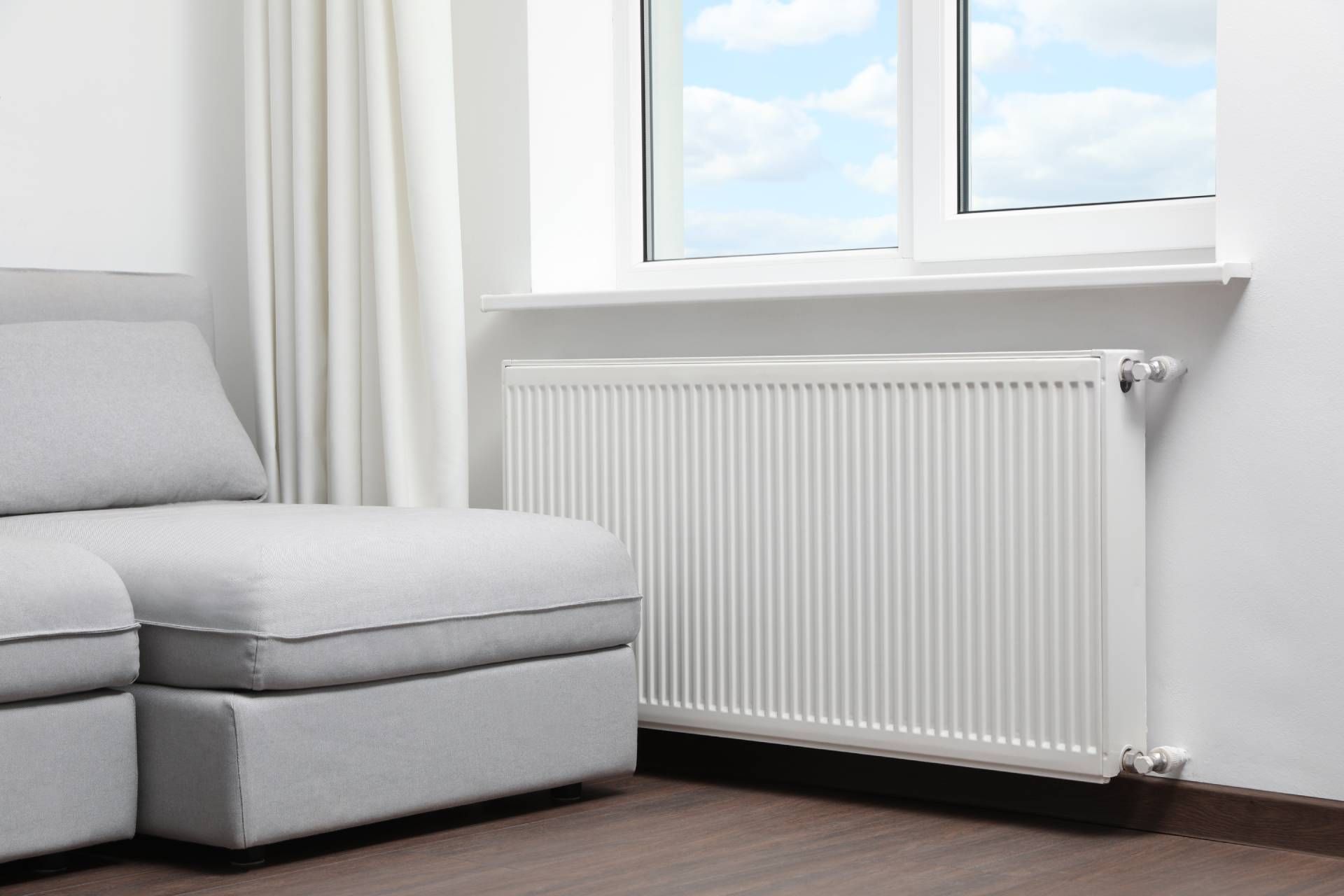 A white radiator next to a window and a light gray sofa.