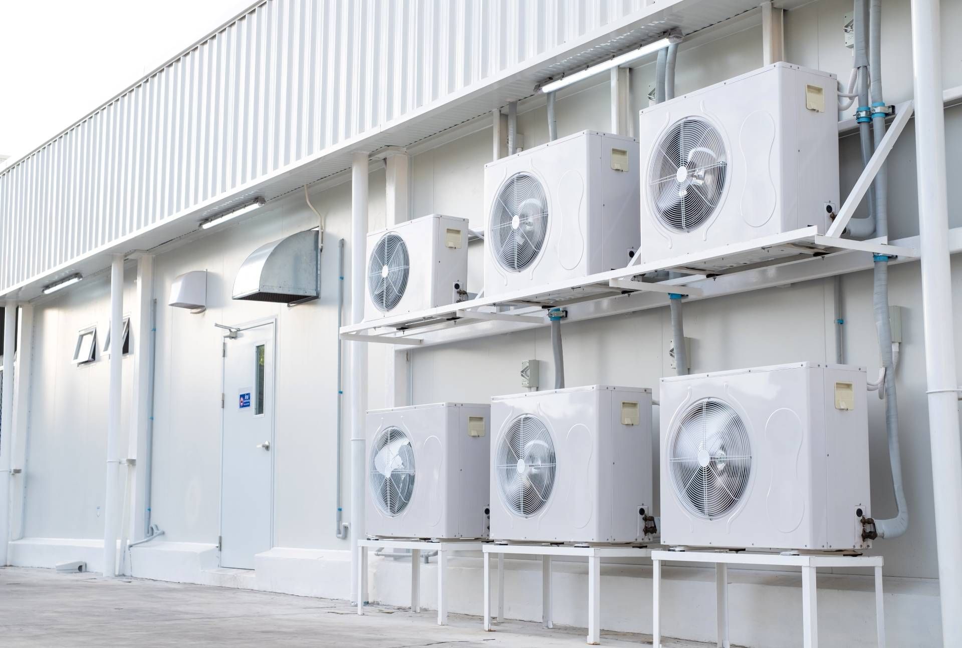 Exterior of a white building with multiple air conditioning units mounted on shelves.