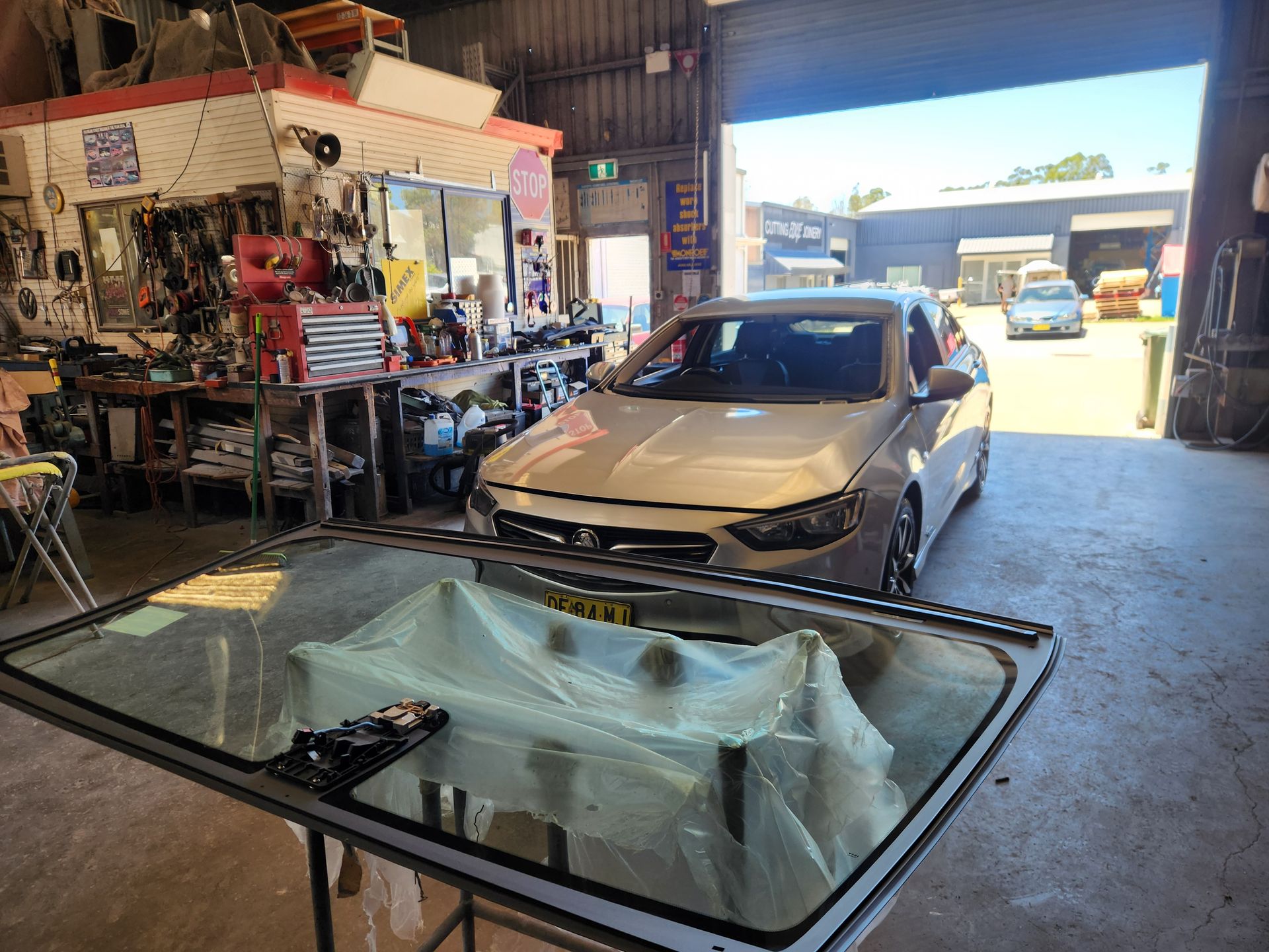 A car is parked in a garage with a windshield sitting on a table.