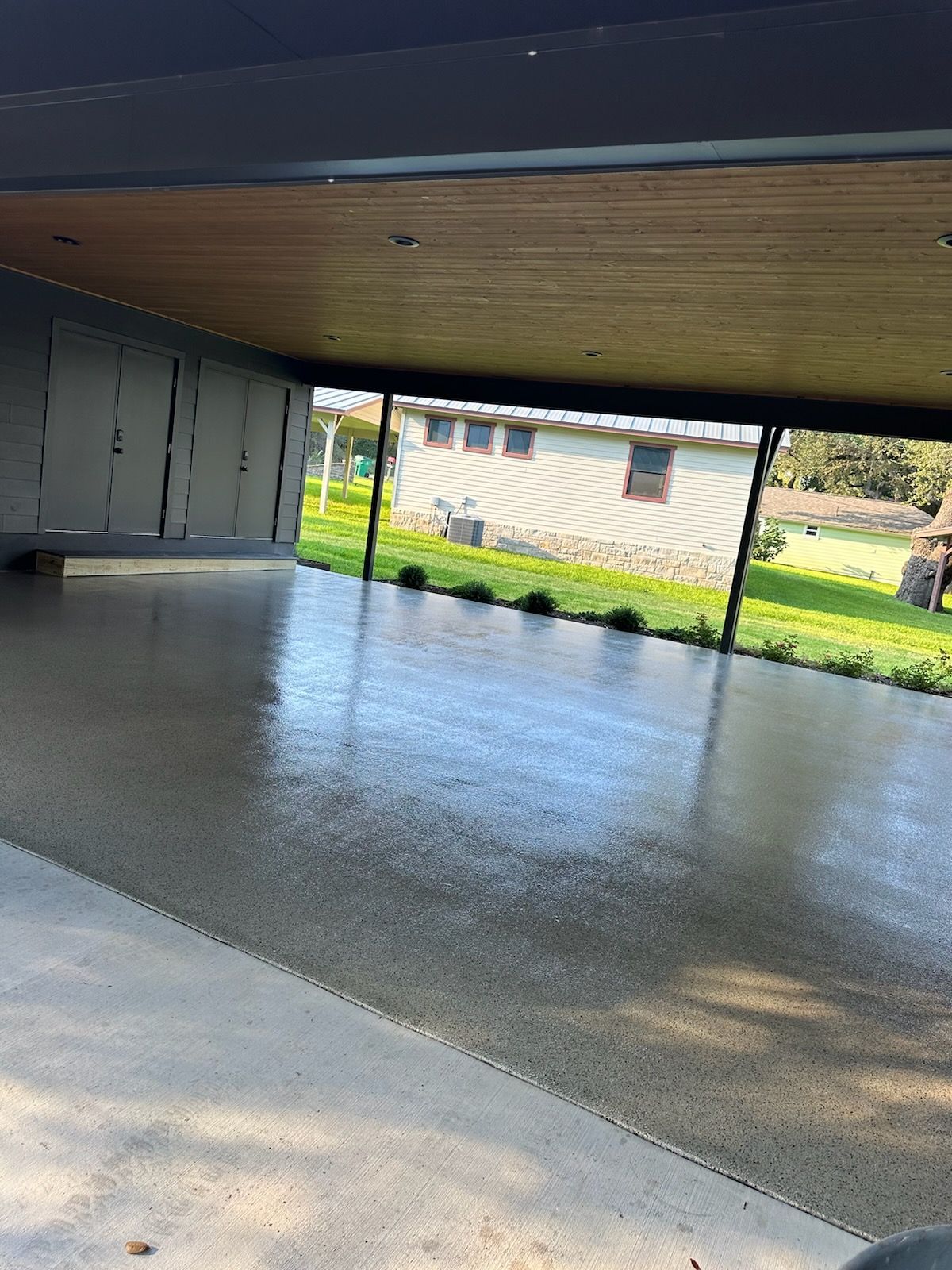A concrete driveway with a wooden ceiling and a house in the background.