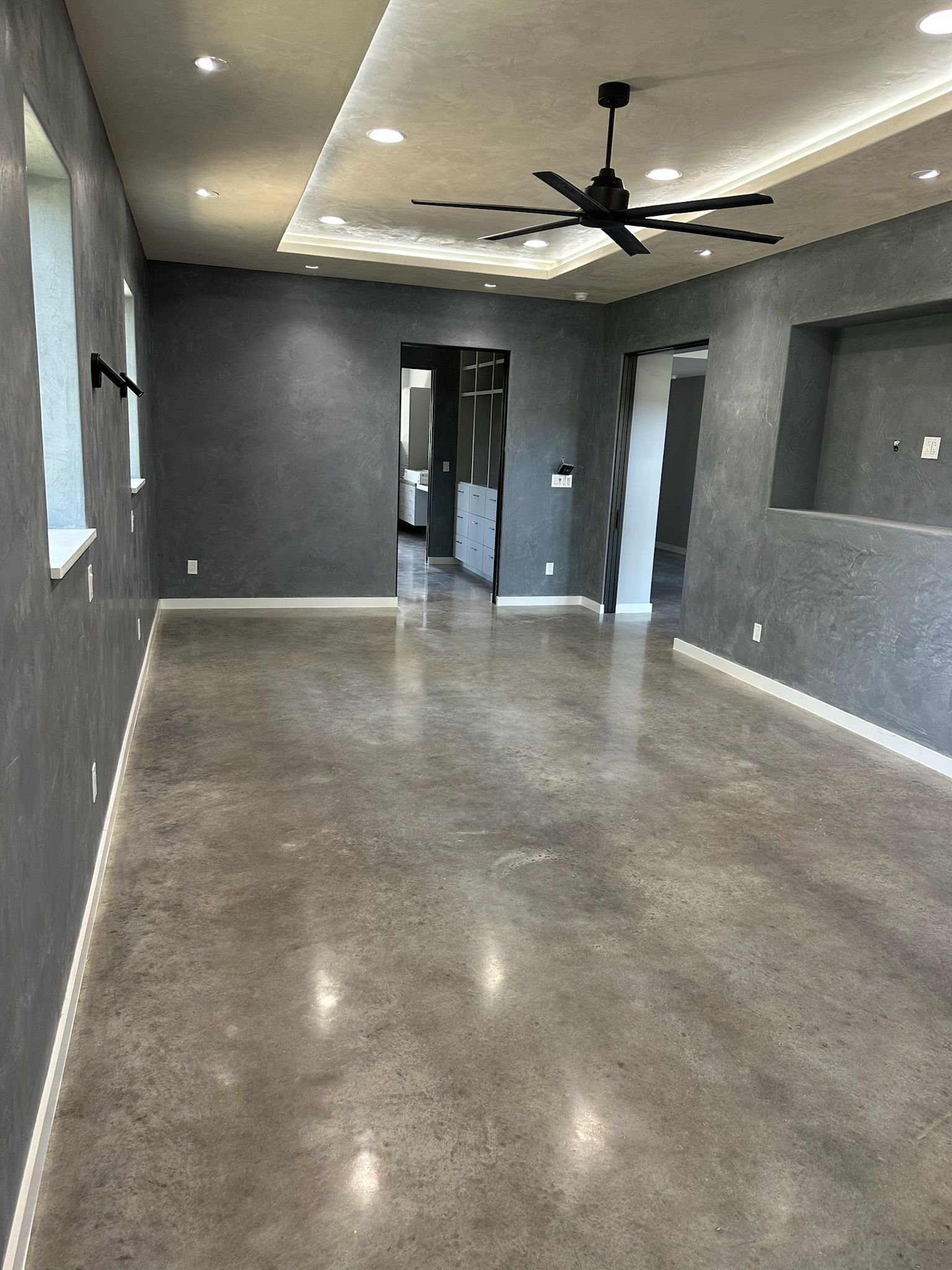 A large empty room with a ceiling fan and a concrete floor.