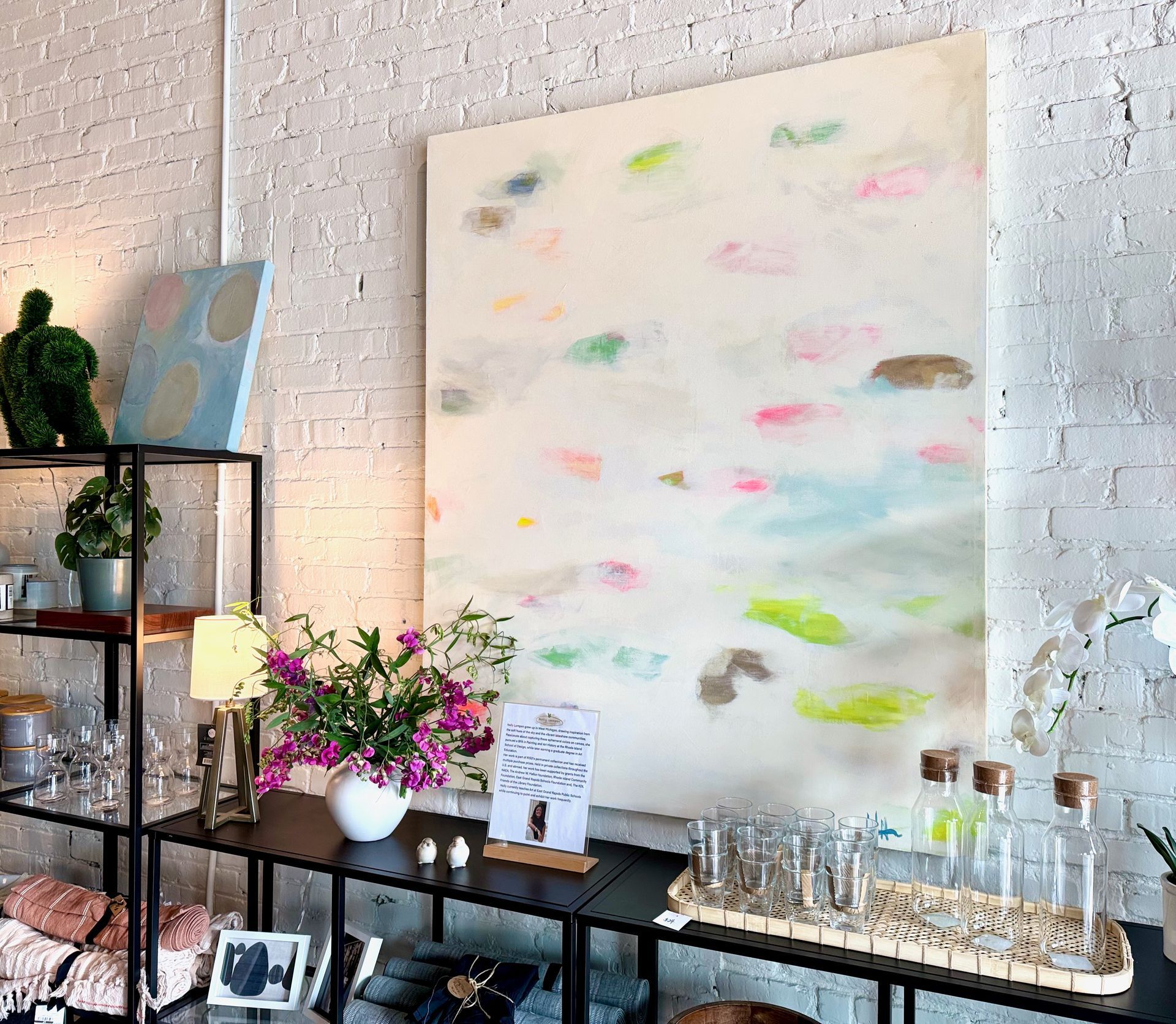 A large abstract painting with bright colors displayed in a store with merchandise on shelves.