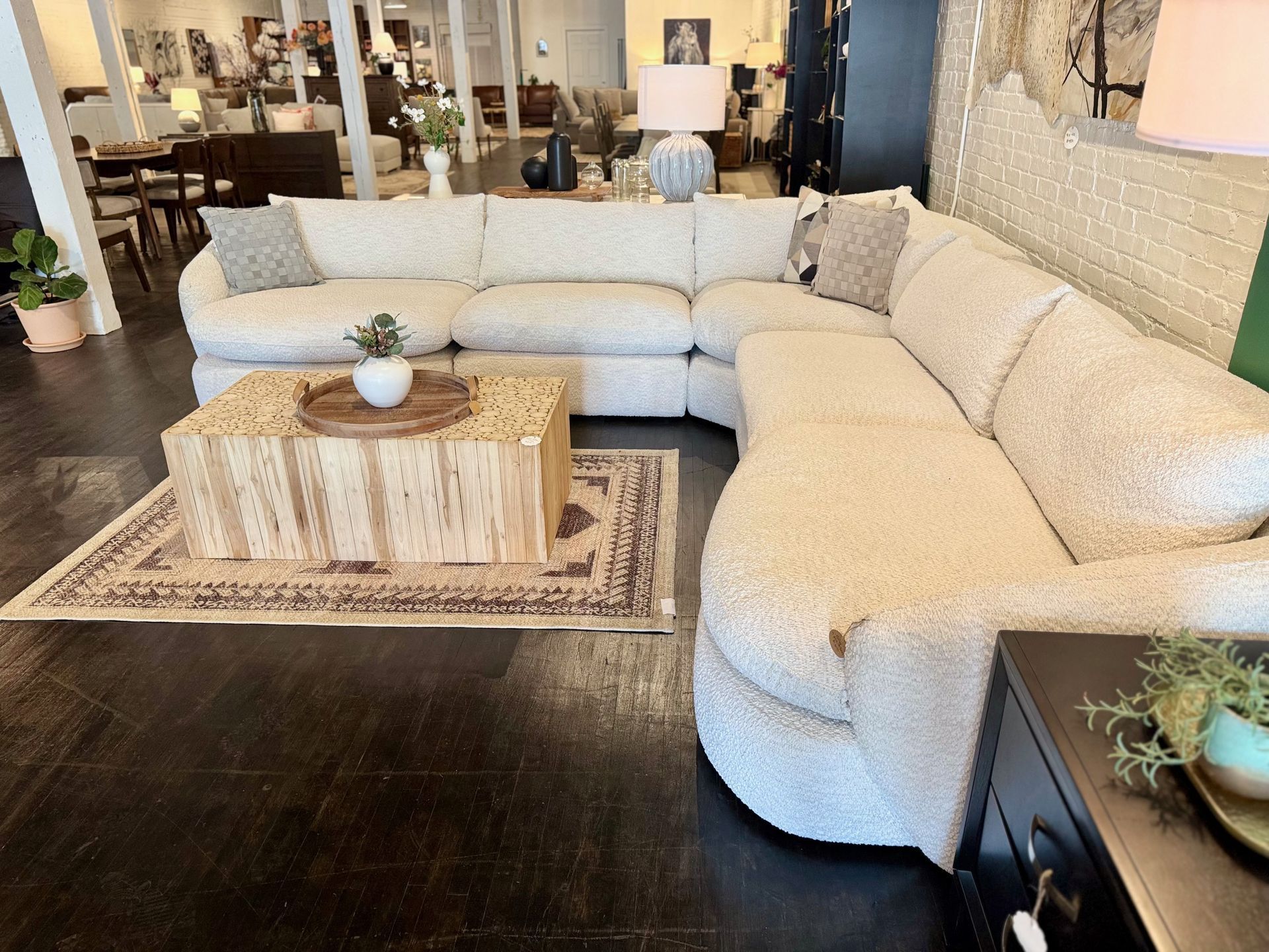 Cream boucle sectional sofa in a showroom with a wooden coffee table and rug.