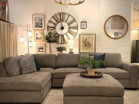 Cozy living room with a gray sectional sofa, ottoman, and gallery wall. Includes a large clock and mirror.